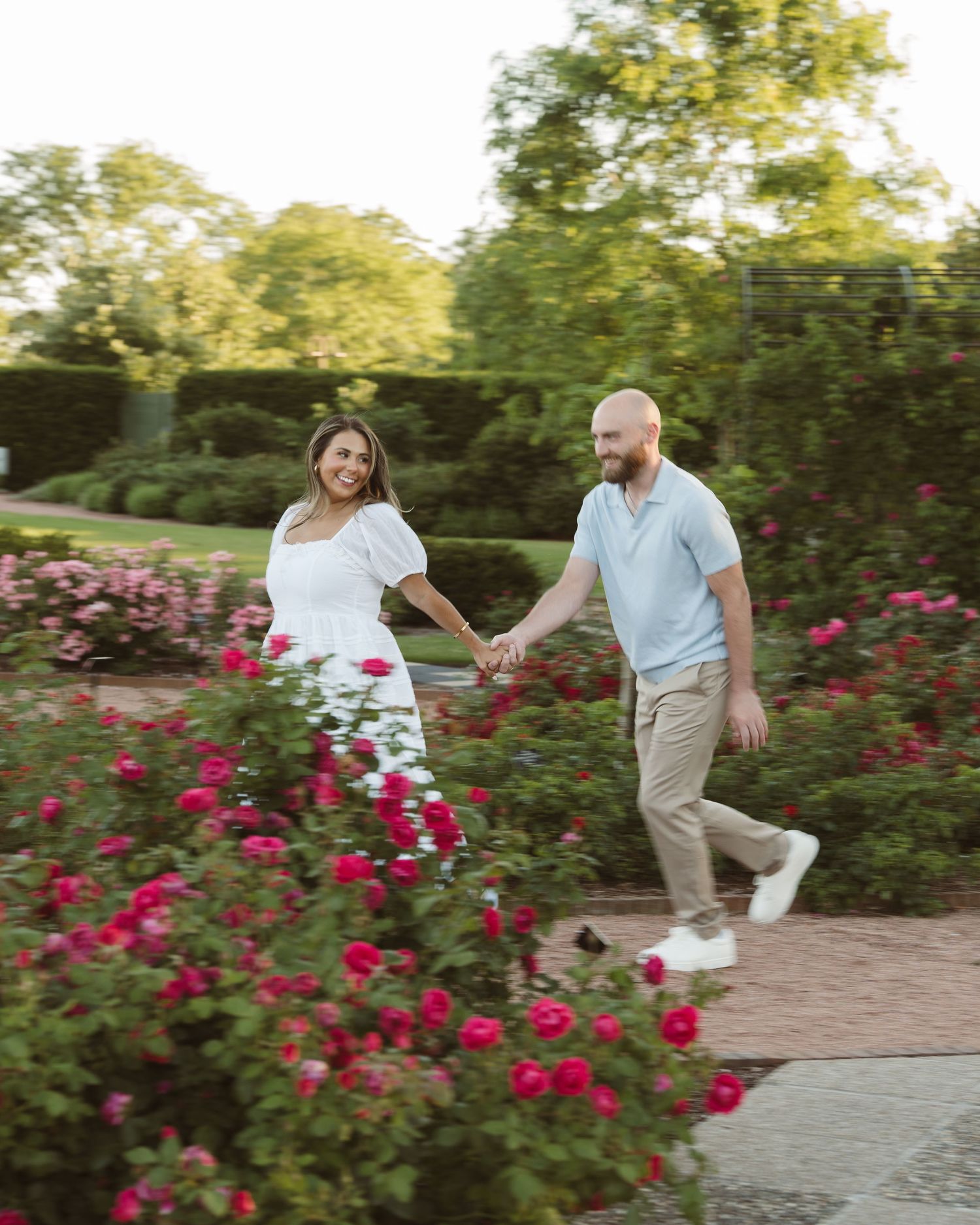 Couple holding hands walking through a rose garden with lush greenery.