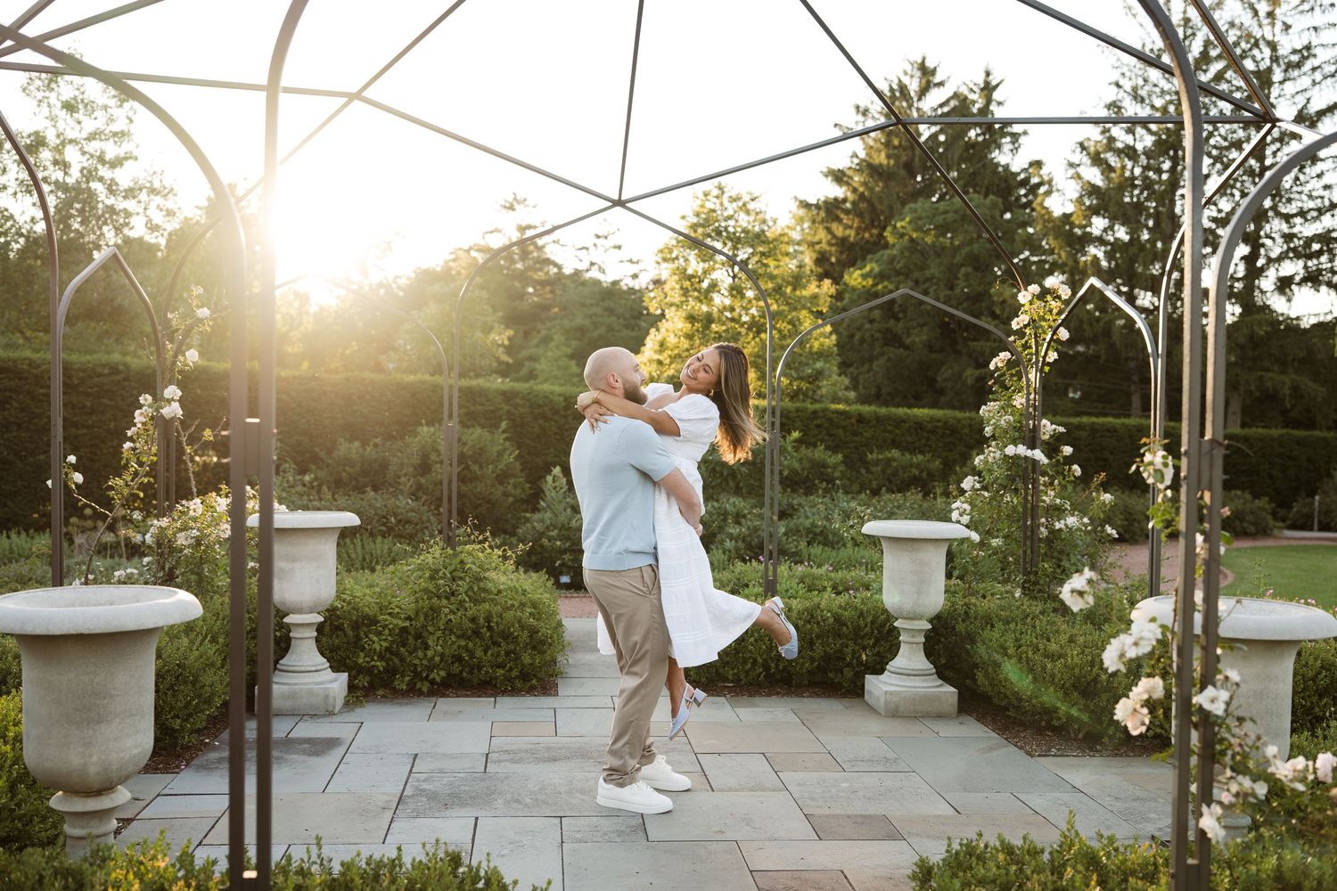 Couple dancing romantically in a sunlit garden gazebo surrounded by roses and lush greenery.