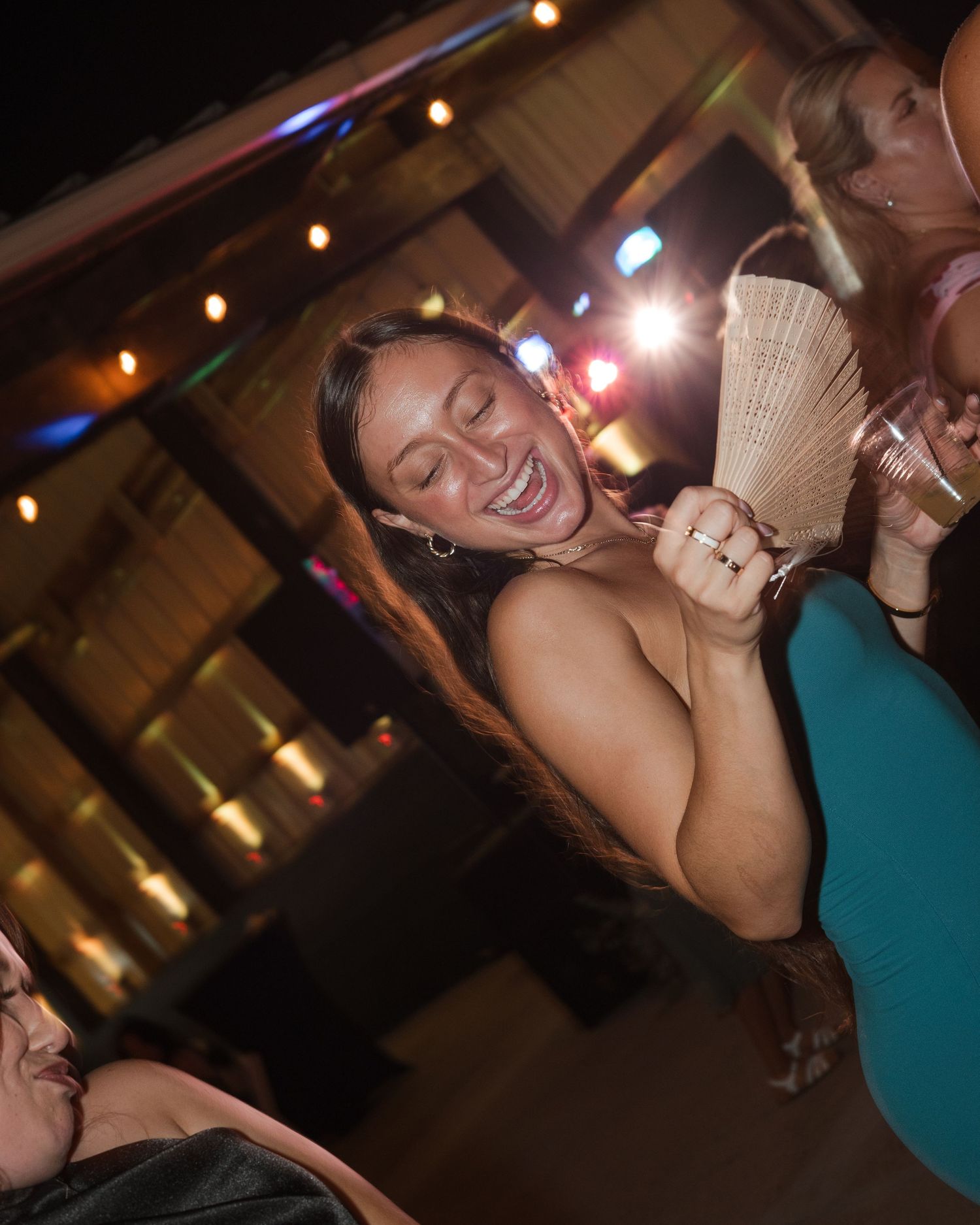 Woman laughing and dancing at an outdoor nightclub party with colorful lights in the background.