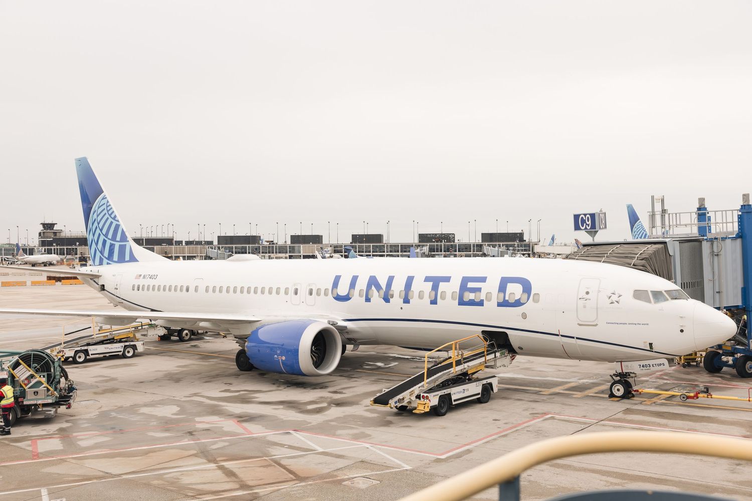 United Airlines Boeing 737 aircraft parked at airport gate on overcast day, ground crew equipment visible nearby.