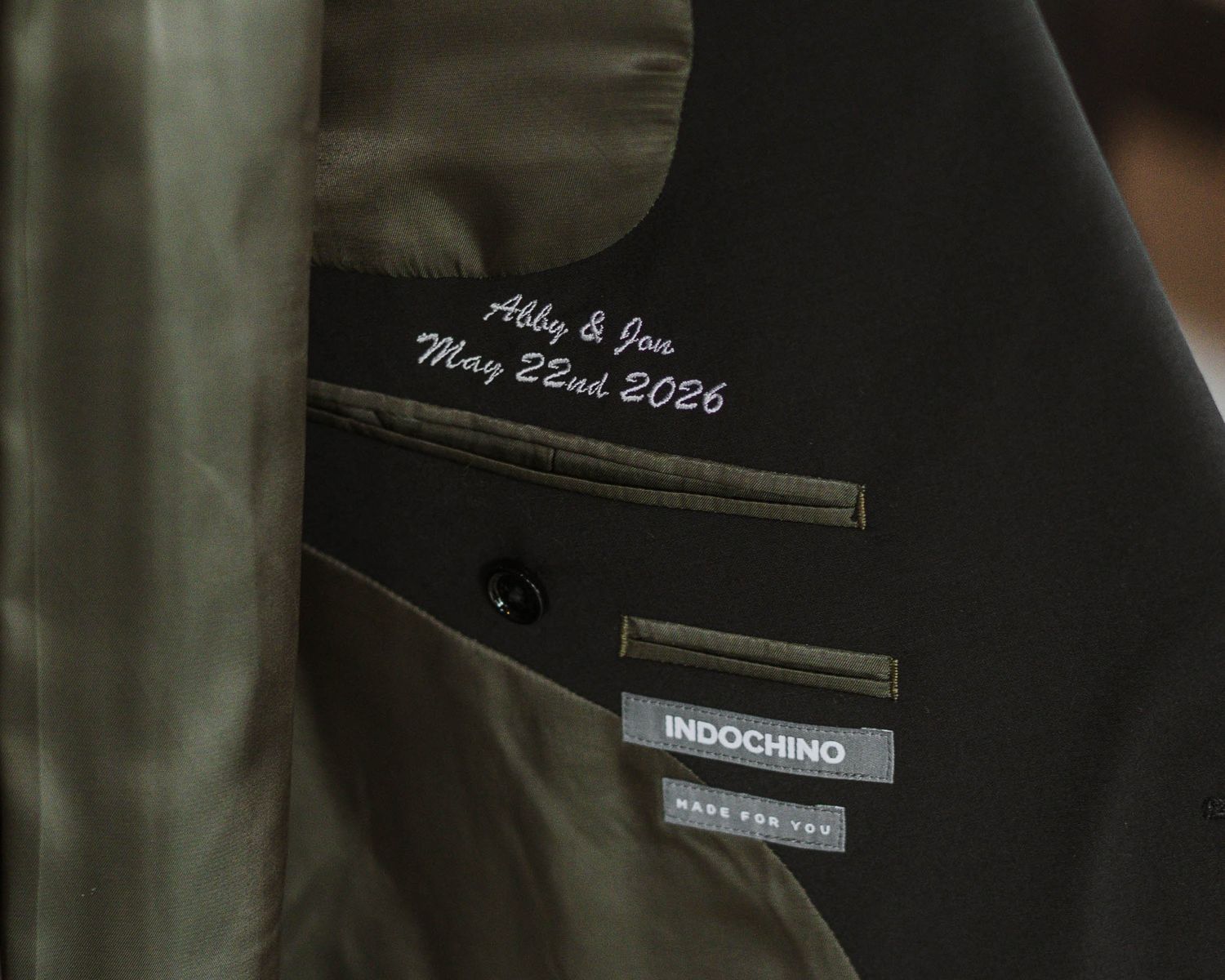 Indochino custom suit jacket with personalized white embroidered label reading Abby & Jen May 22nd 2026.