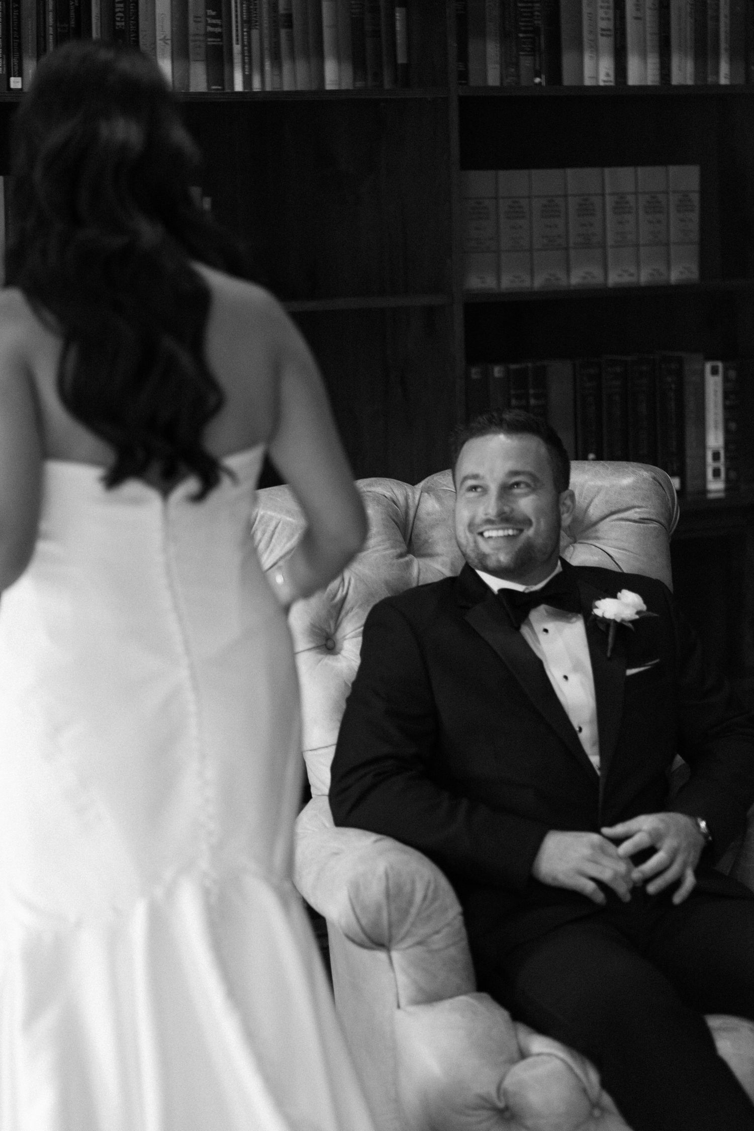 Black and white photo of a groom smiling at his bride in a wedding dress during a first look moment.