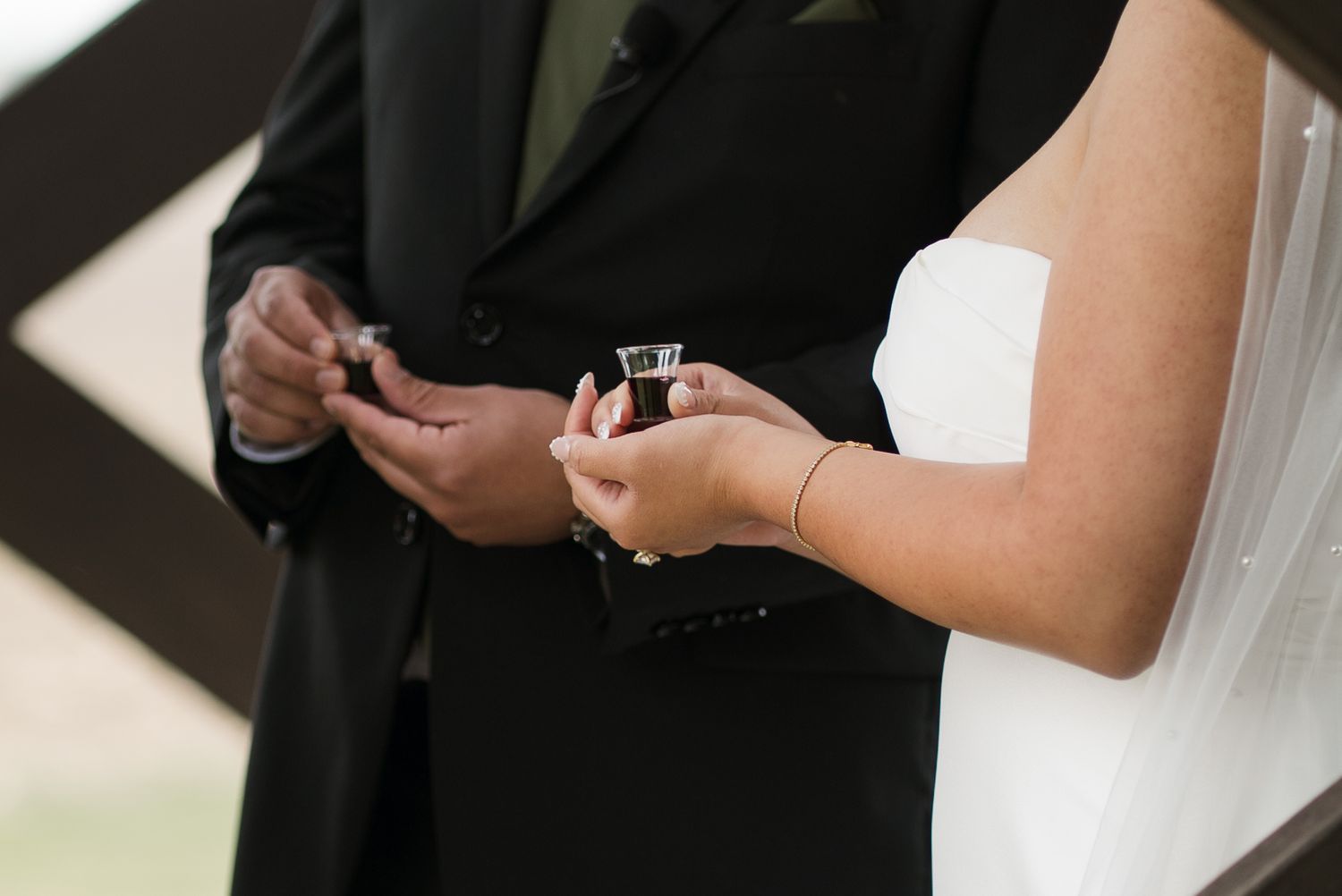 Bride and groom exchanging rings during wedding ceremony, close-up of hands holding small communion cups.