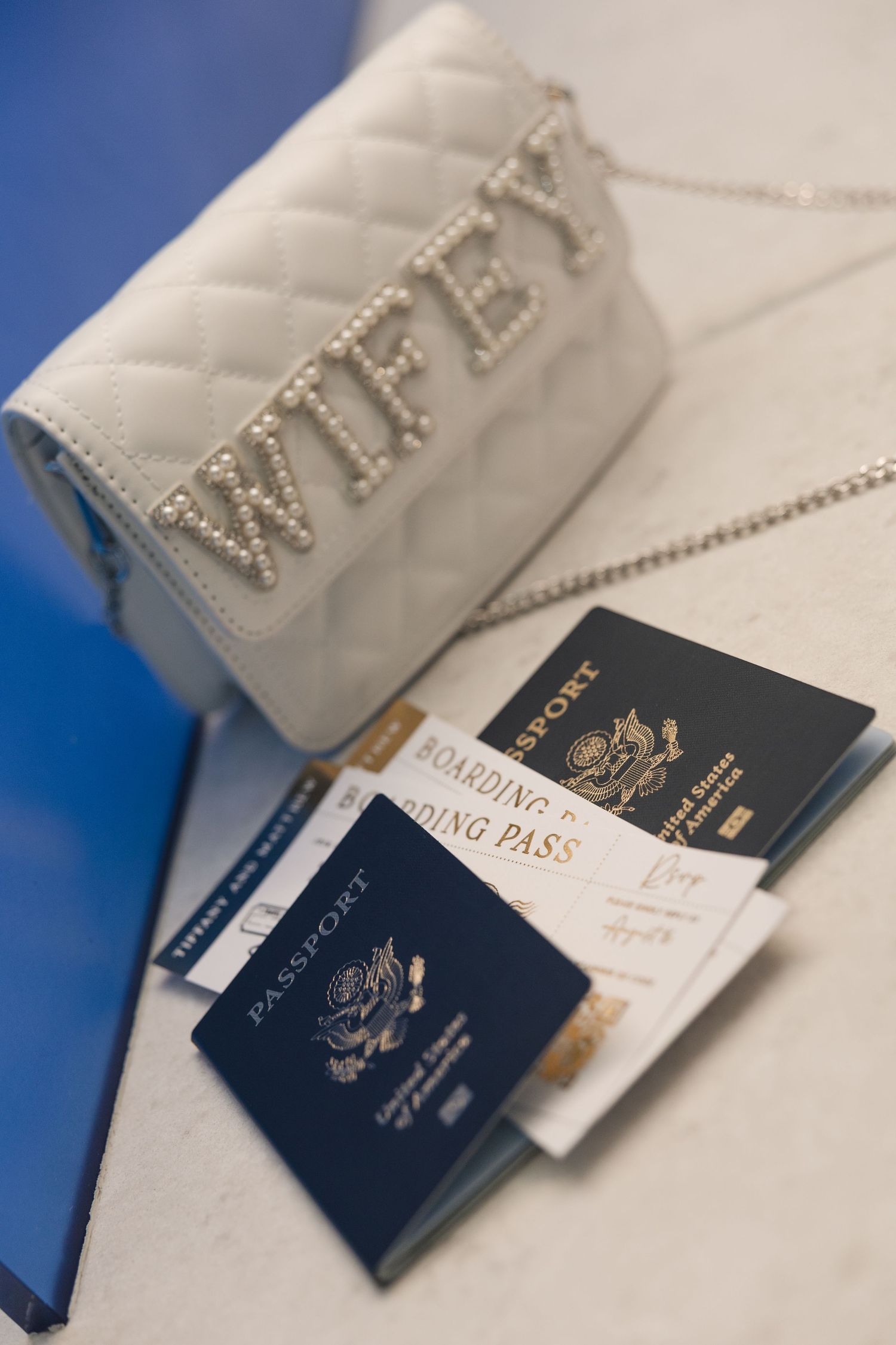 White quilted WIFEY purse with pearl letters beside two US passports and boarding passes on a surface.