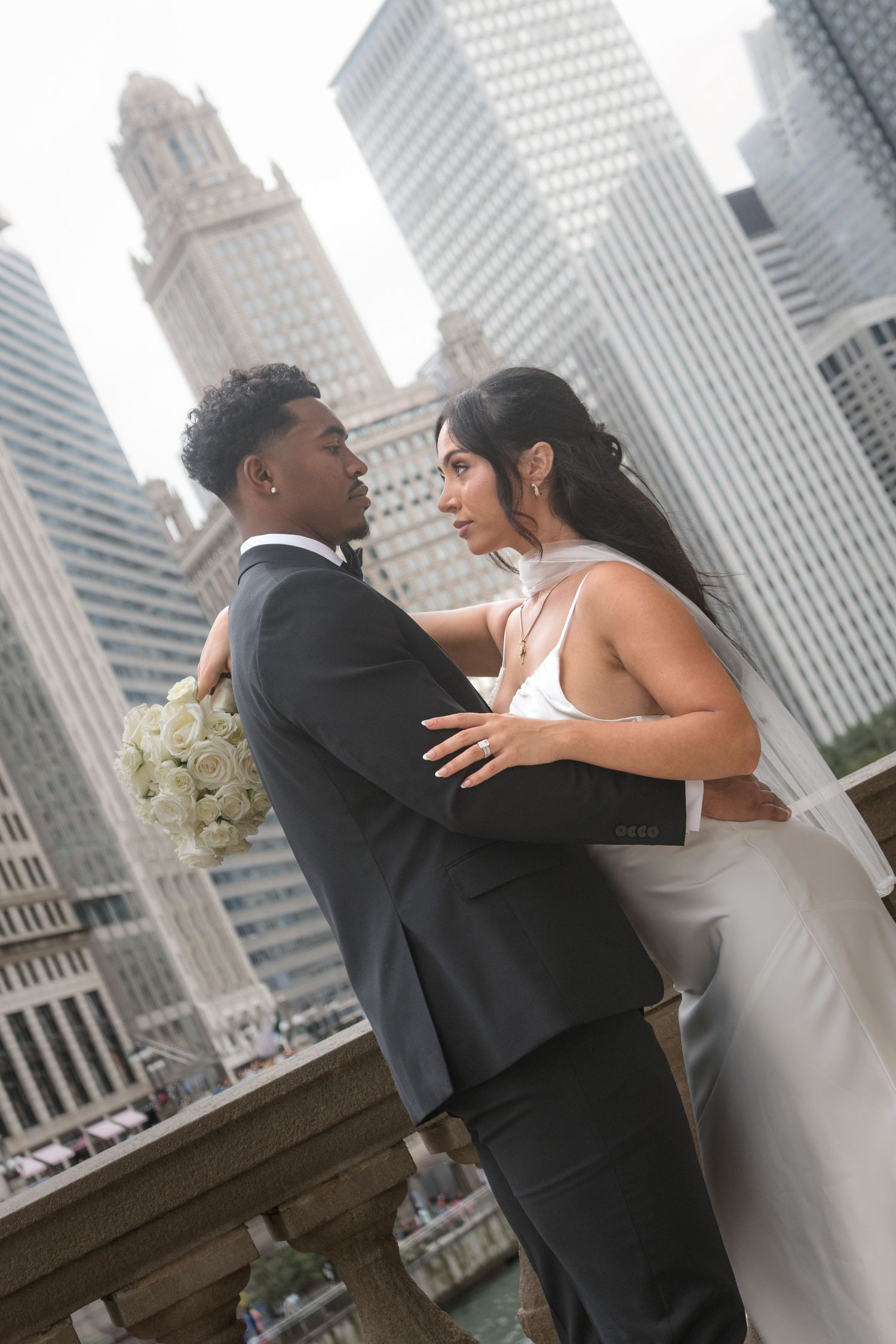 Interracial couple in wedding attire embracing with Chicago skyline skyscrapers in the background.