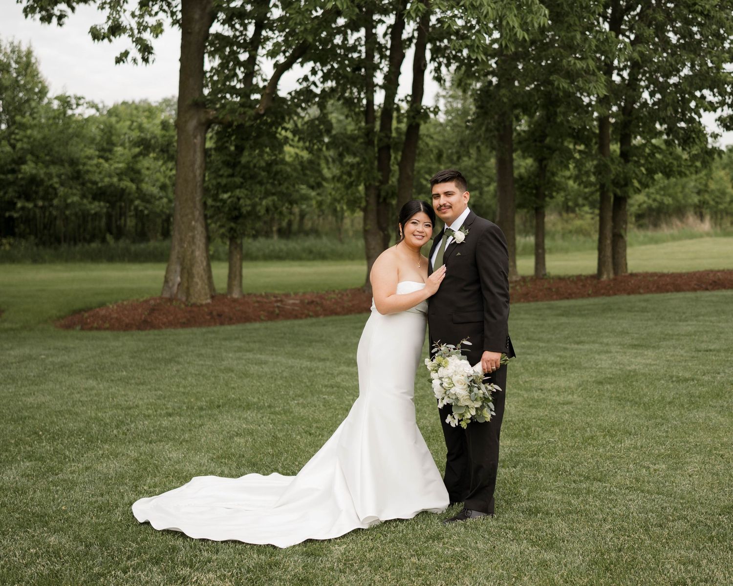 Bride and groom portrait on lush green lawn, bride in mermaid gown with long train.