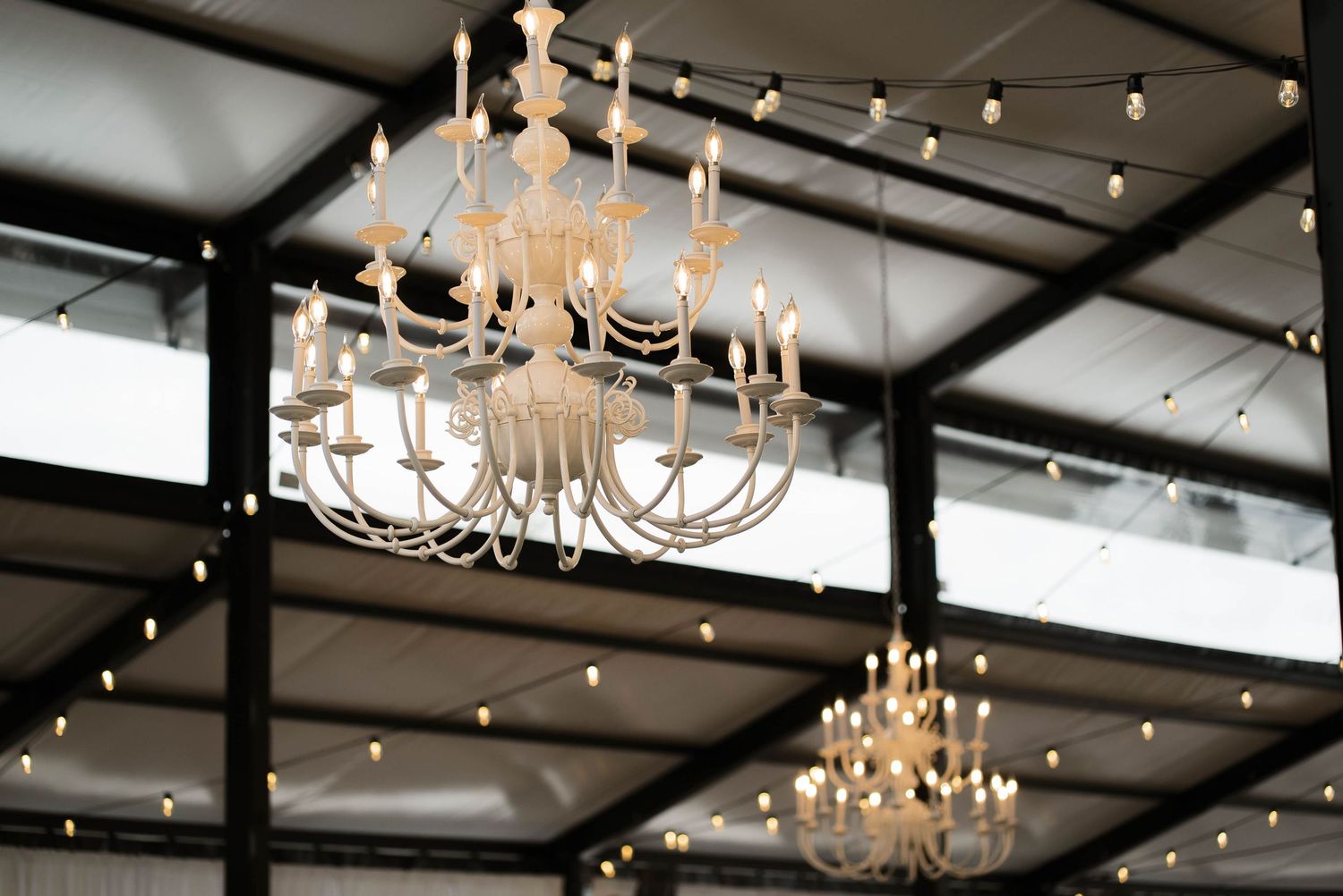 Ornate gold chandeliers and string lights hanging from a black ceiling at a wedding venue.