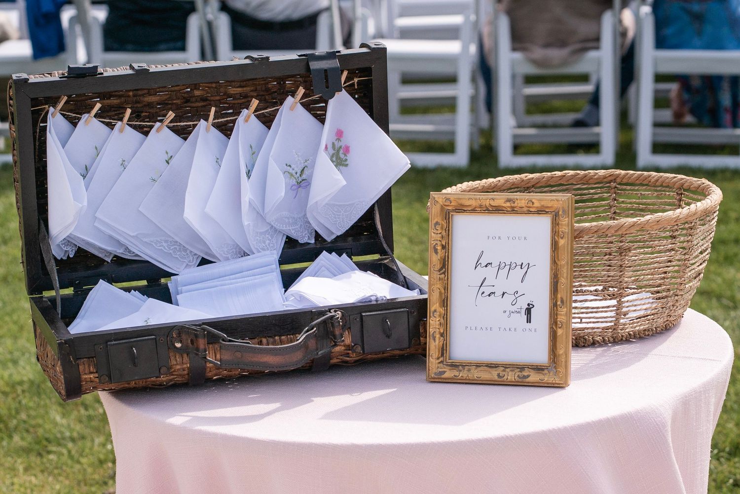 Wedding reception details featuring elegant place cards, woven baskets, and white decorative elements on display outdoors.
