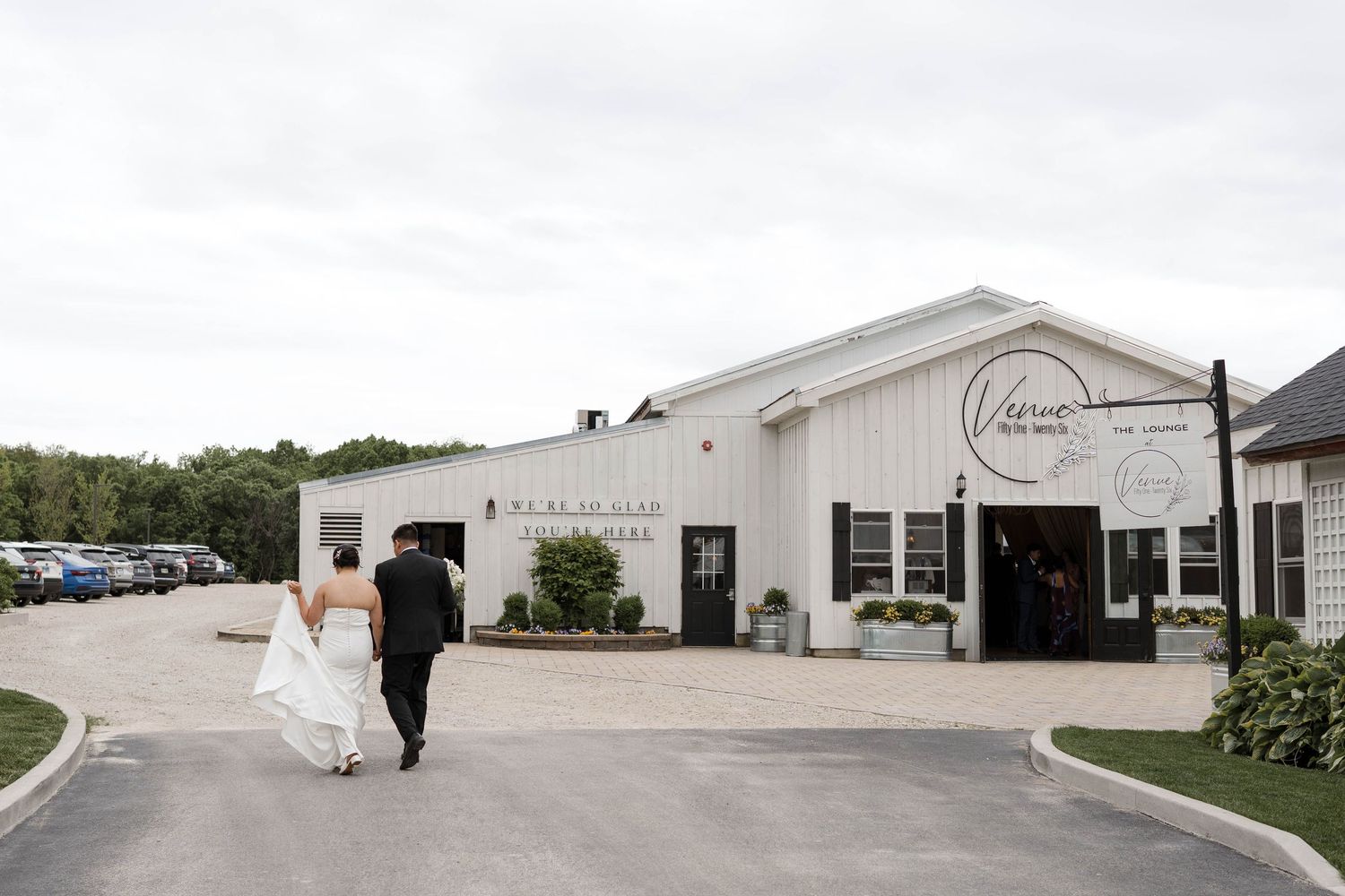 Bride and groom walking toward white barn wedding venue on overcast day.