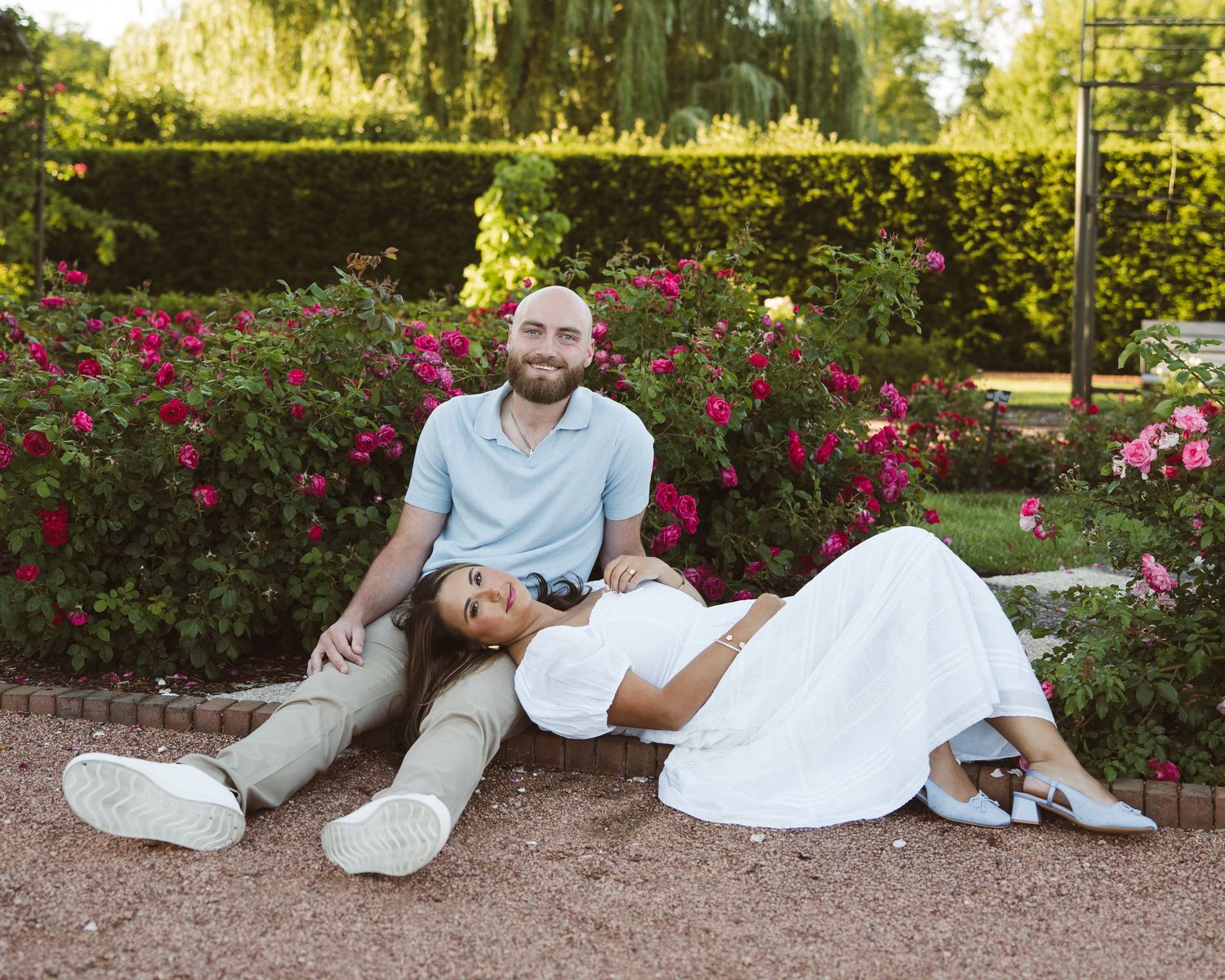 Engaged couple relaxing together in a colorful rose garden.
