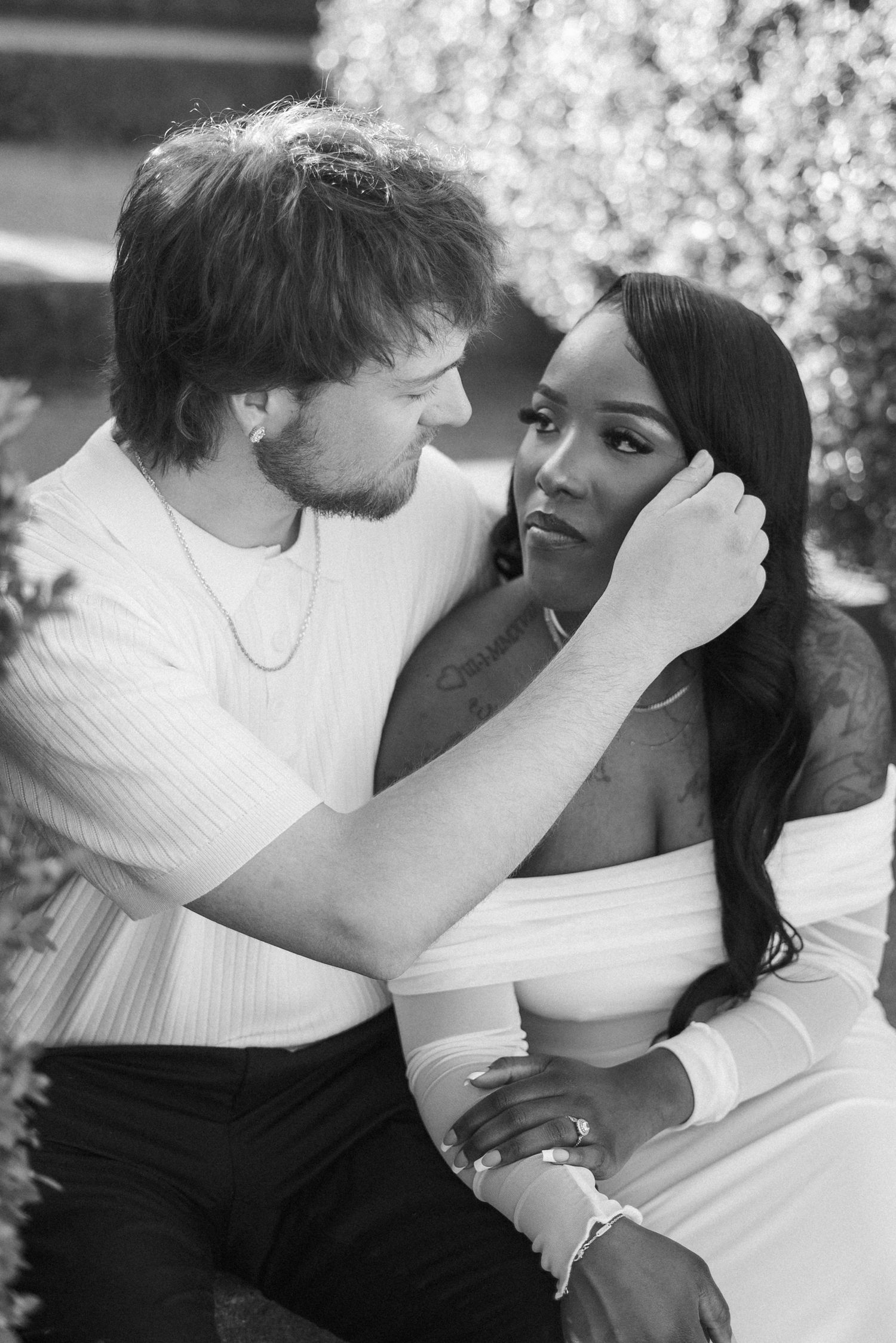 Black and white photo of an interracial couple sharing a tender moment outdoors, man gently touching womans face.