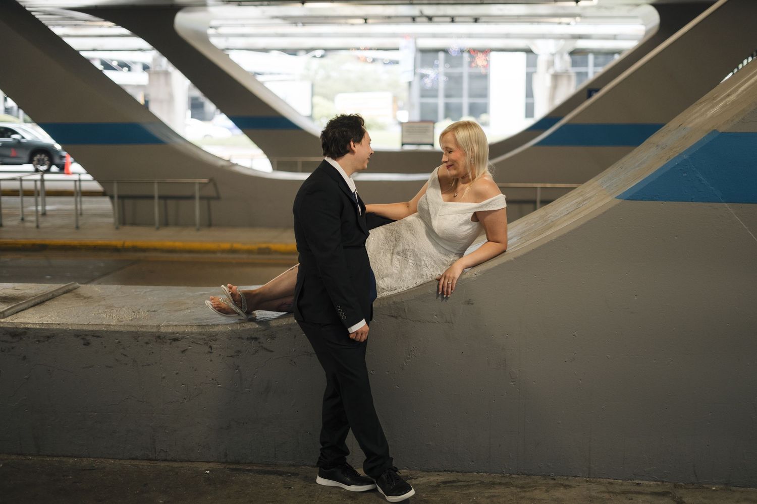 Couple in wedding attire sharing a romantic moment in an urban parking garage setting.