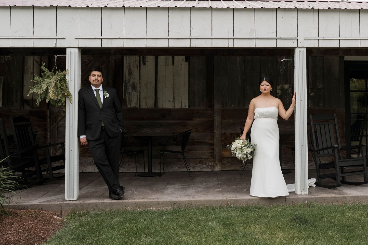 A bride and groom stand apart on a rustic barn porch during their first look moment.