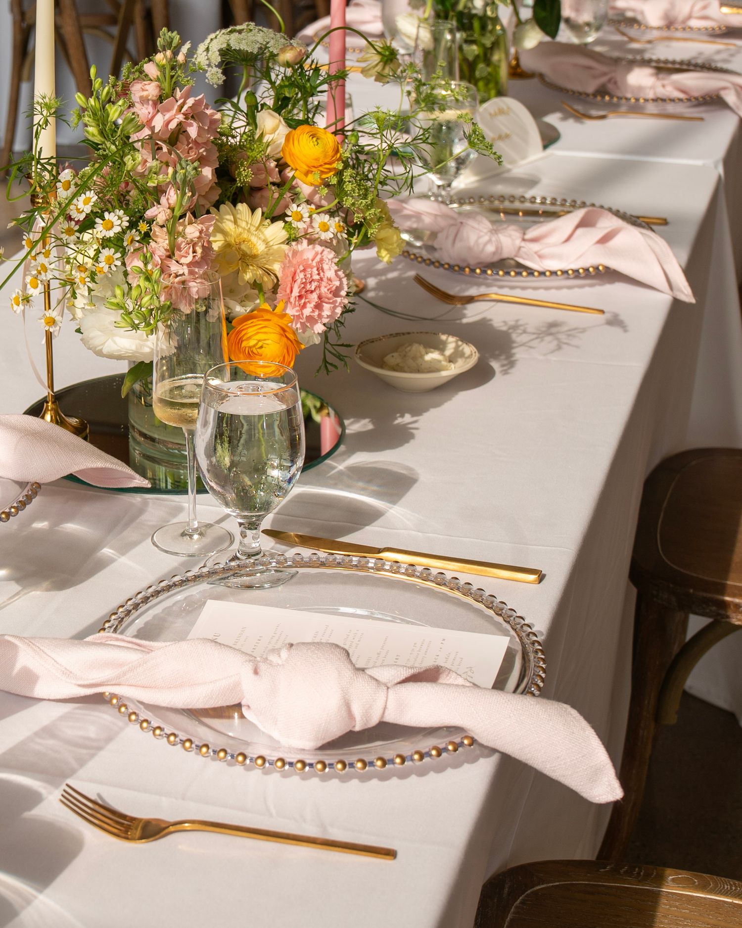 Elegant wedding reception table setting with gold charger plates, white linens, and delicate floral centerpieces.