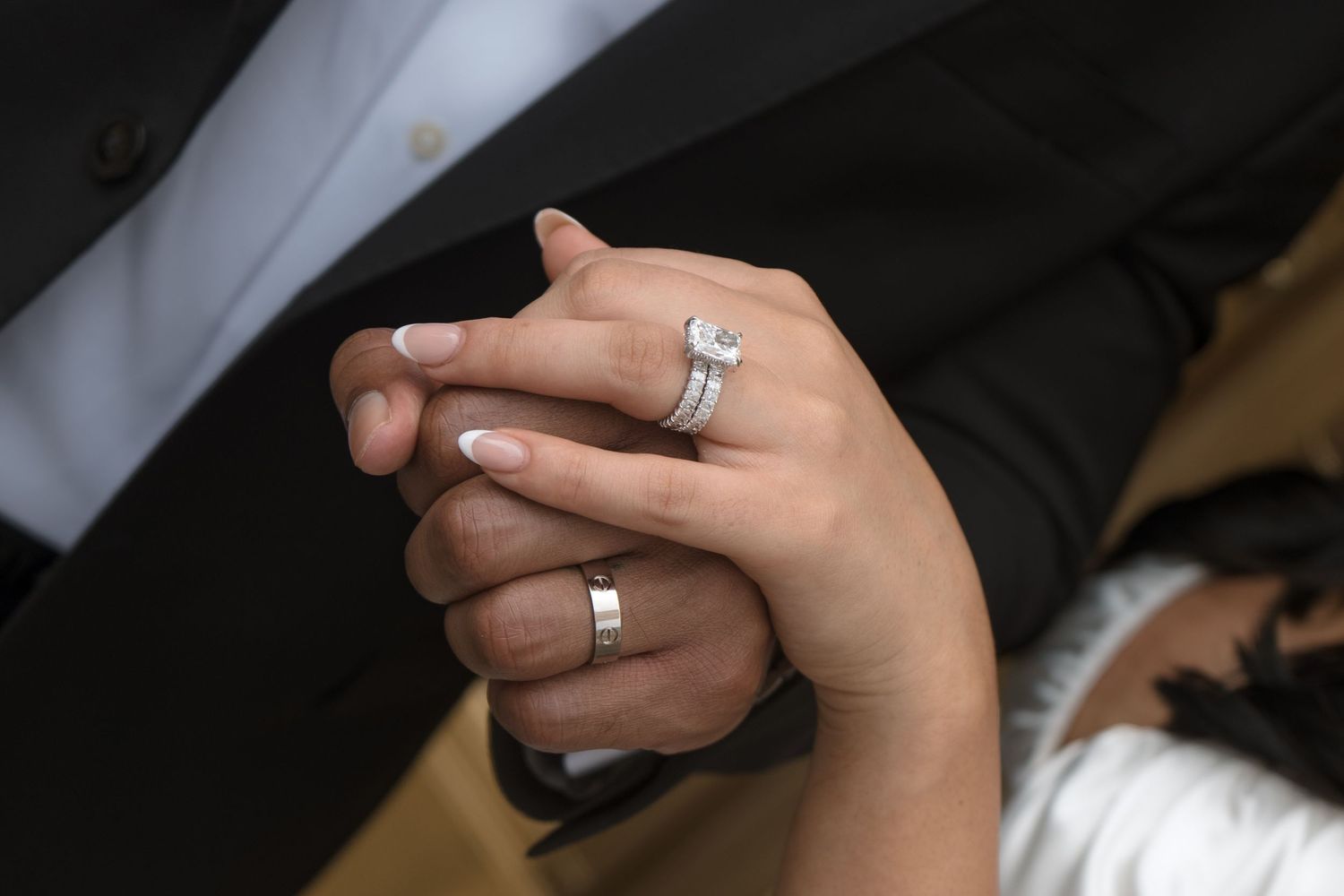 Close-up of a bride and groom holding hands, showcasing a diamond engagement ring and wedding band.