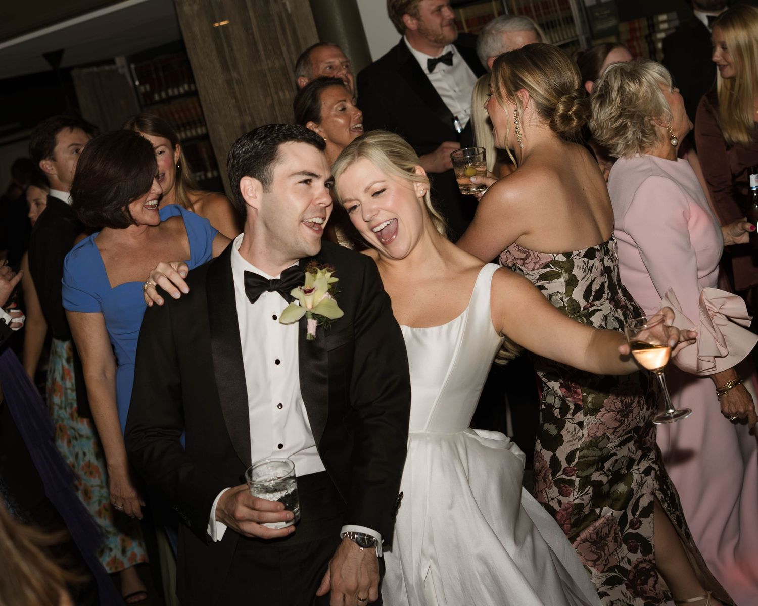 Joyful bride and groom dancing and laughing together at their wedding reception surrounded by guests.