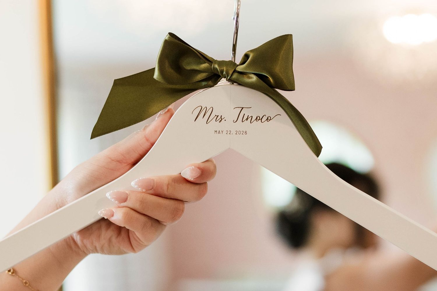 Personalized white wedding hanger with olive green bow reading Mrs Tinoco, held by bride on wedding day.