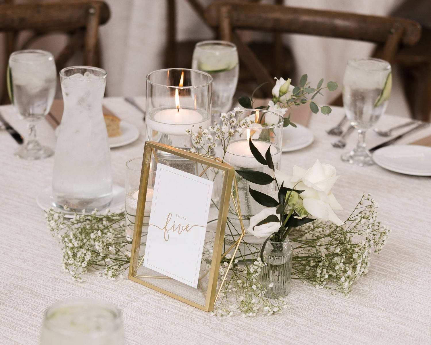 Gold-framed table number five centerpiece with white roses, baby's breath, and candles at an elegant wedding reception.