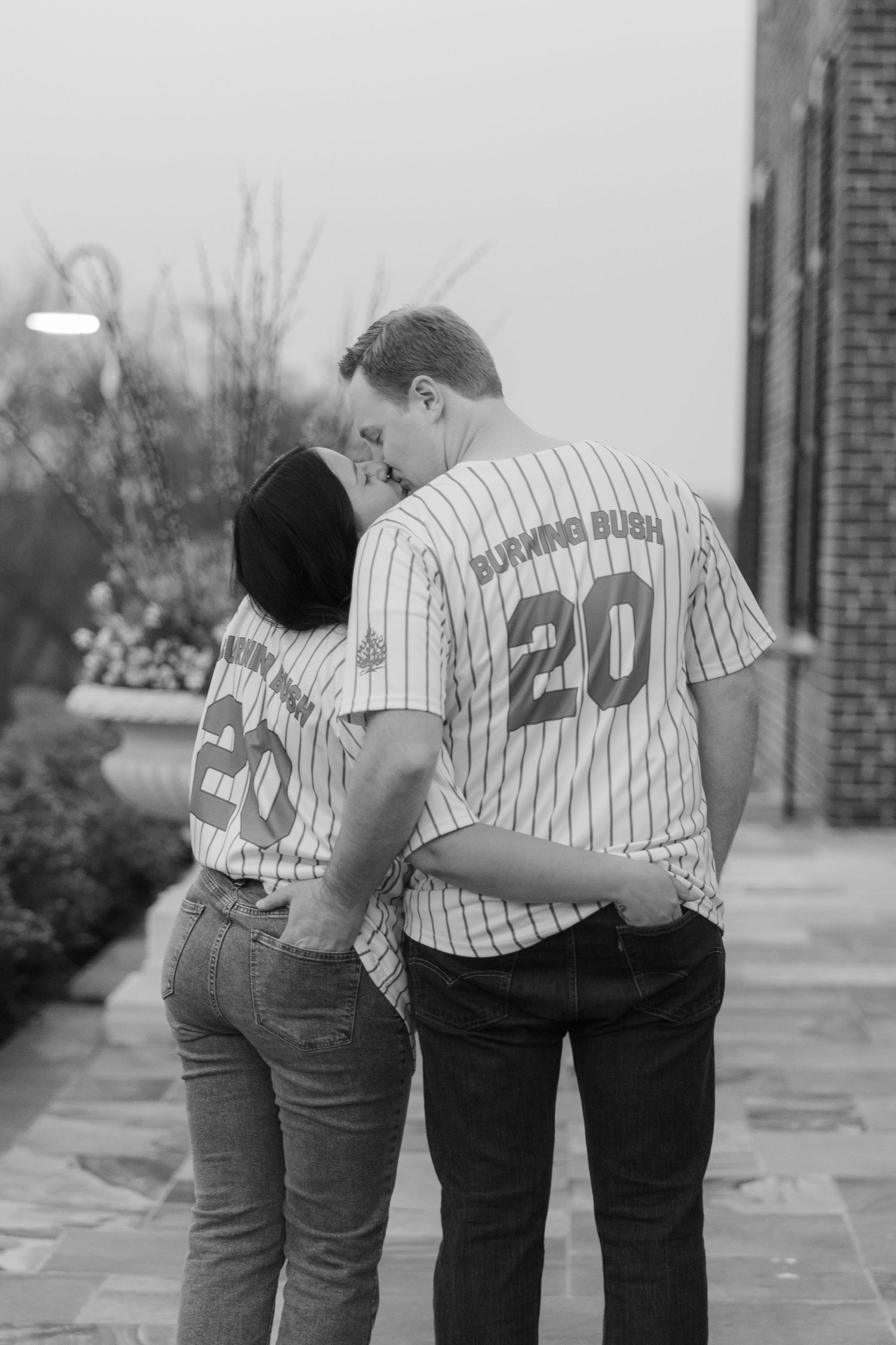 Couple kissing in matching number 20 pinstripe baseball jerseys, black and white photo taken from behind.