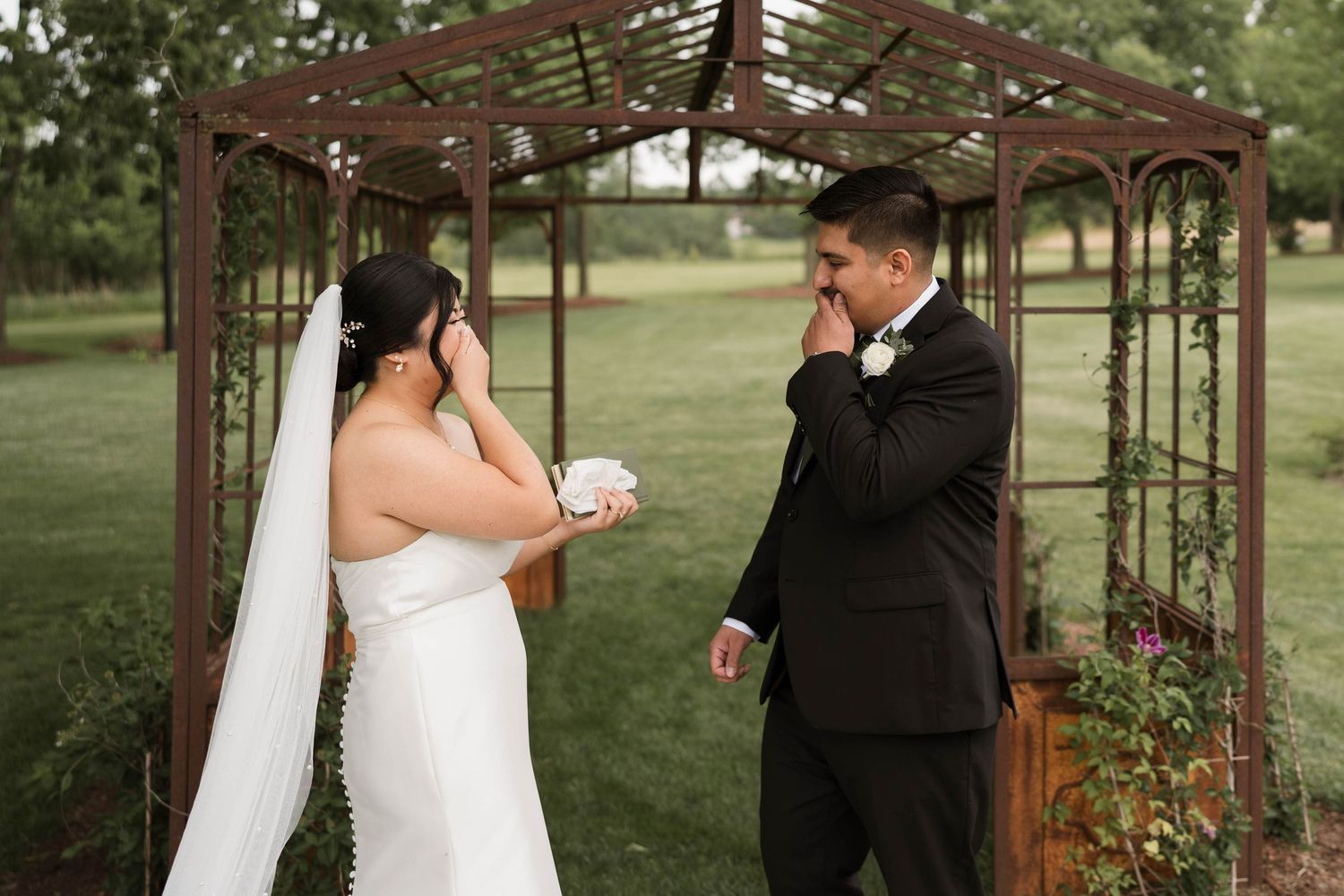 Emotional bride and groom sharing a first look moment under a rustic garden arbor.