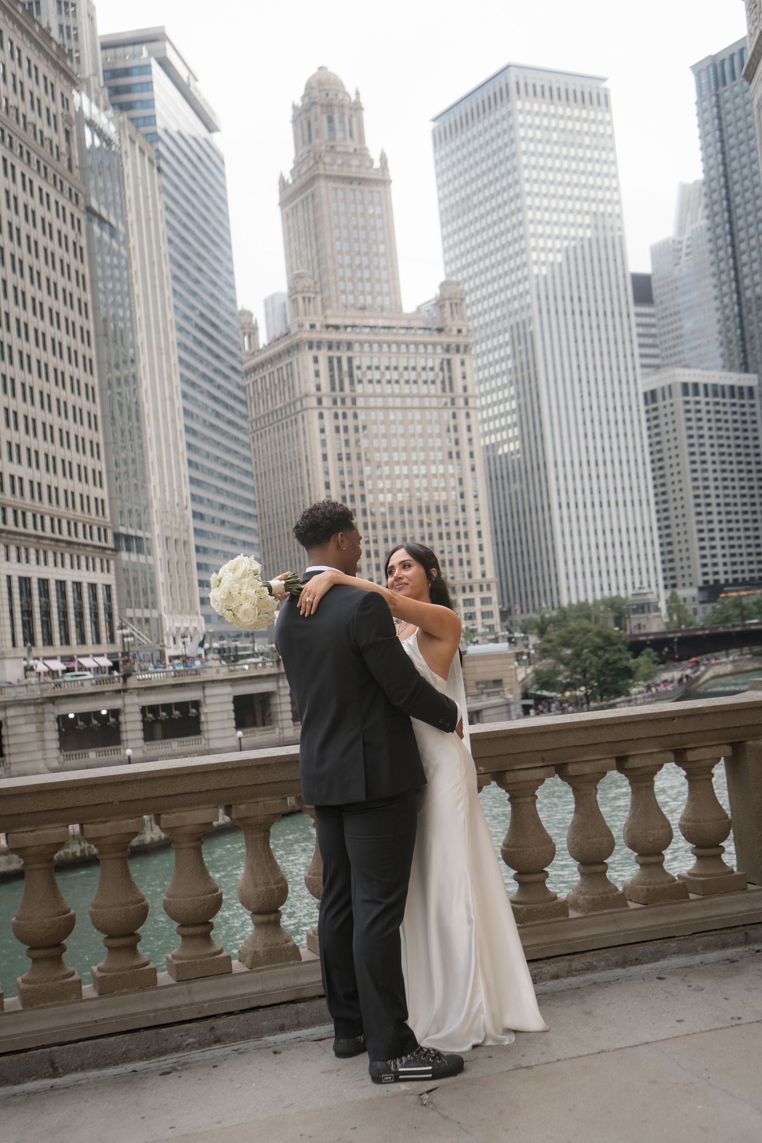 Bride and groom dancing on Chicago Riverwalk terrace with iconic city skyline and river in background.