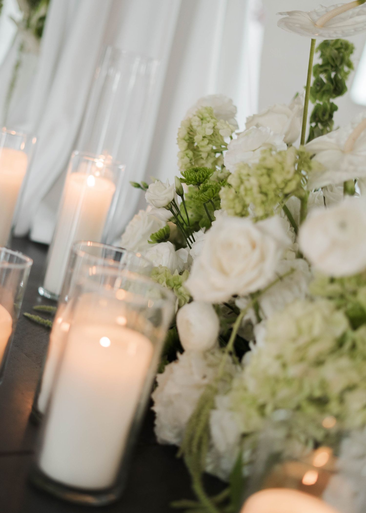 Elegant wedding table with white roses, hydrangeas, and glowing pillar candles creating a romantic floral centerpiece.
