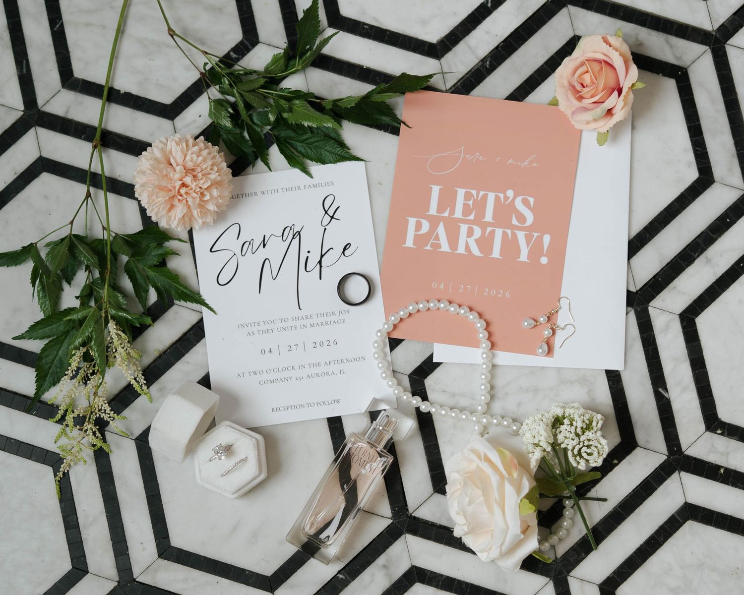 Wedding invitation suite for Sara and Mike with a pink party card, pearl jewelry, rings, and floral accents on geometric tile.