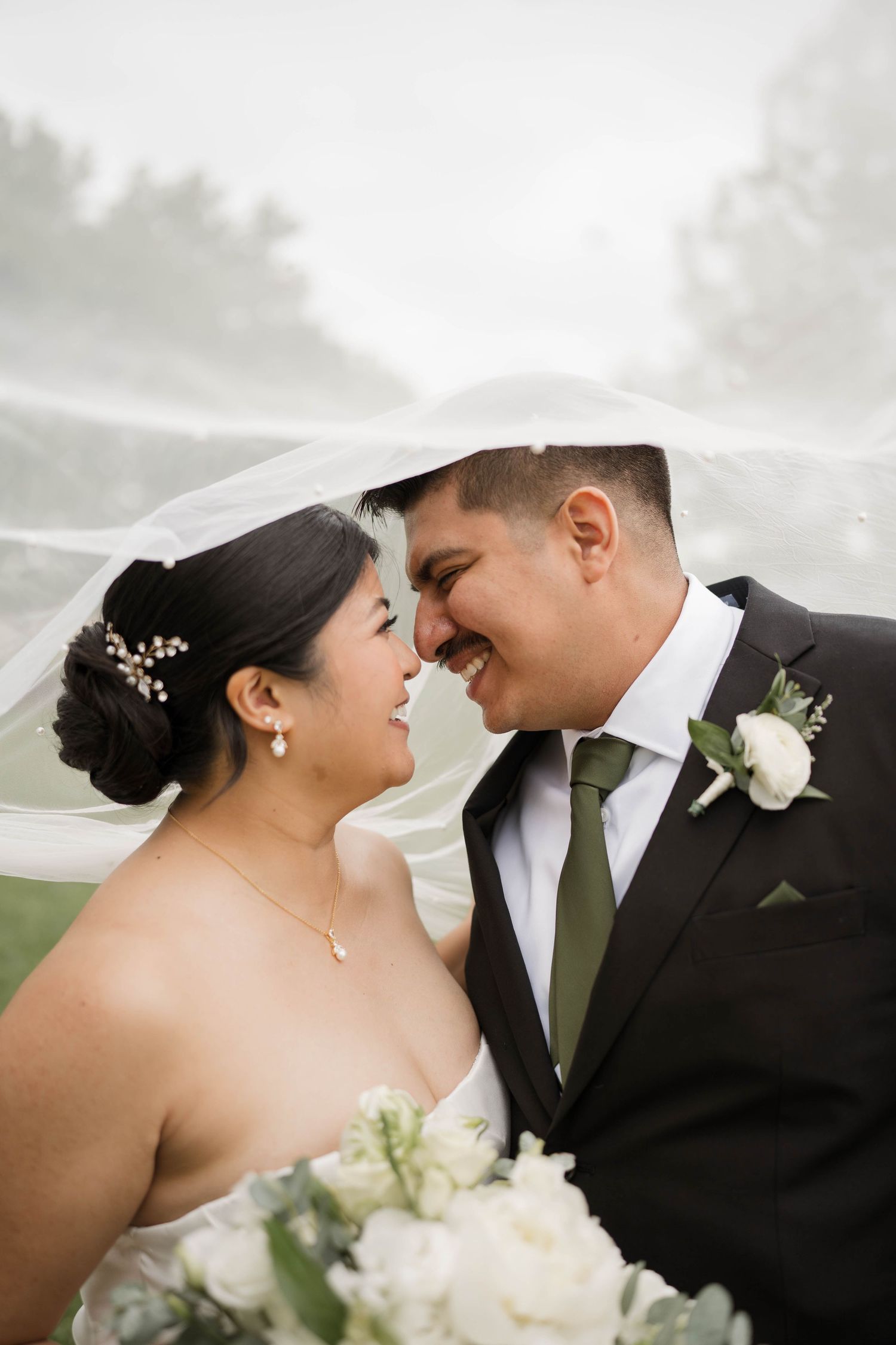 Bride and groom sharing an intimate moment under a flowing veil with white floral bouquet.