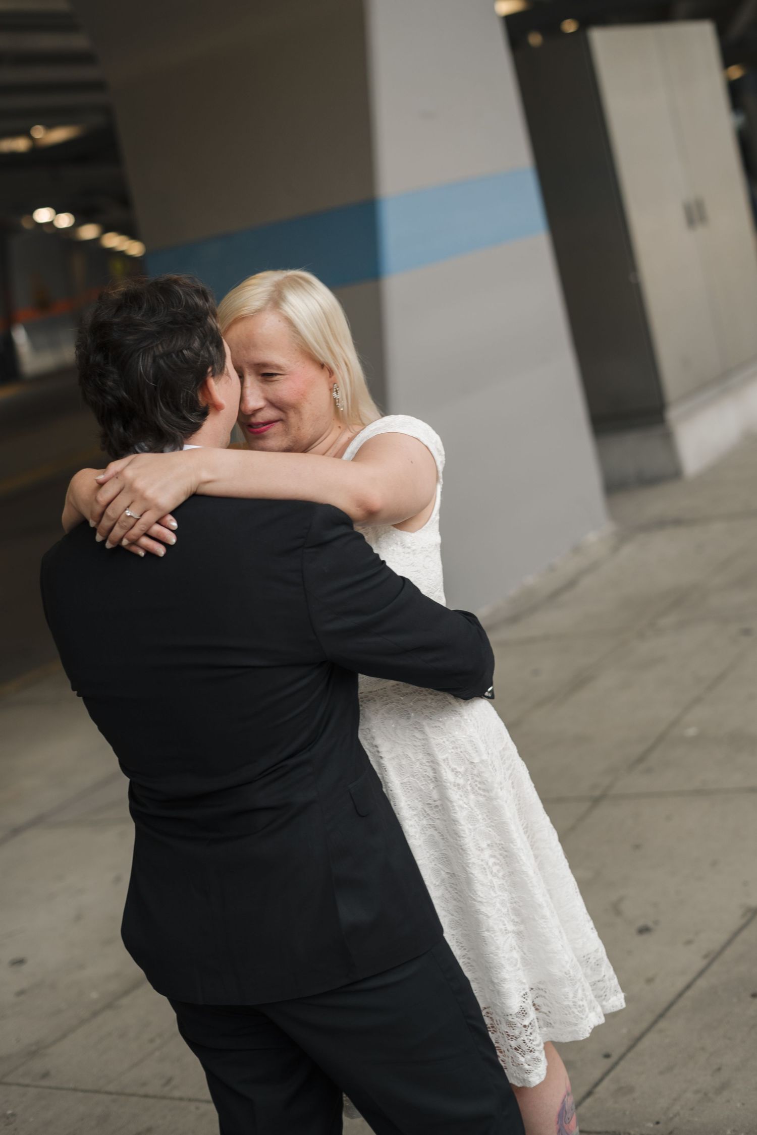 Newlyweds sharing a romantic embrace outdoors, bride in white lace dress smiling.