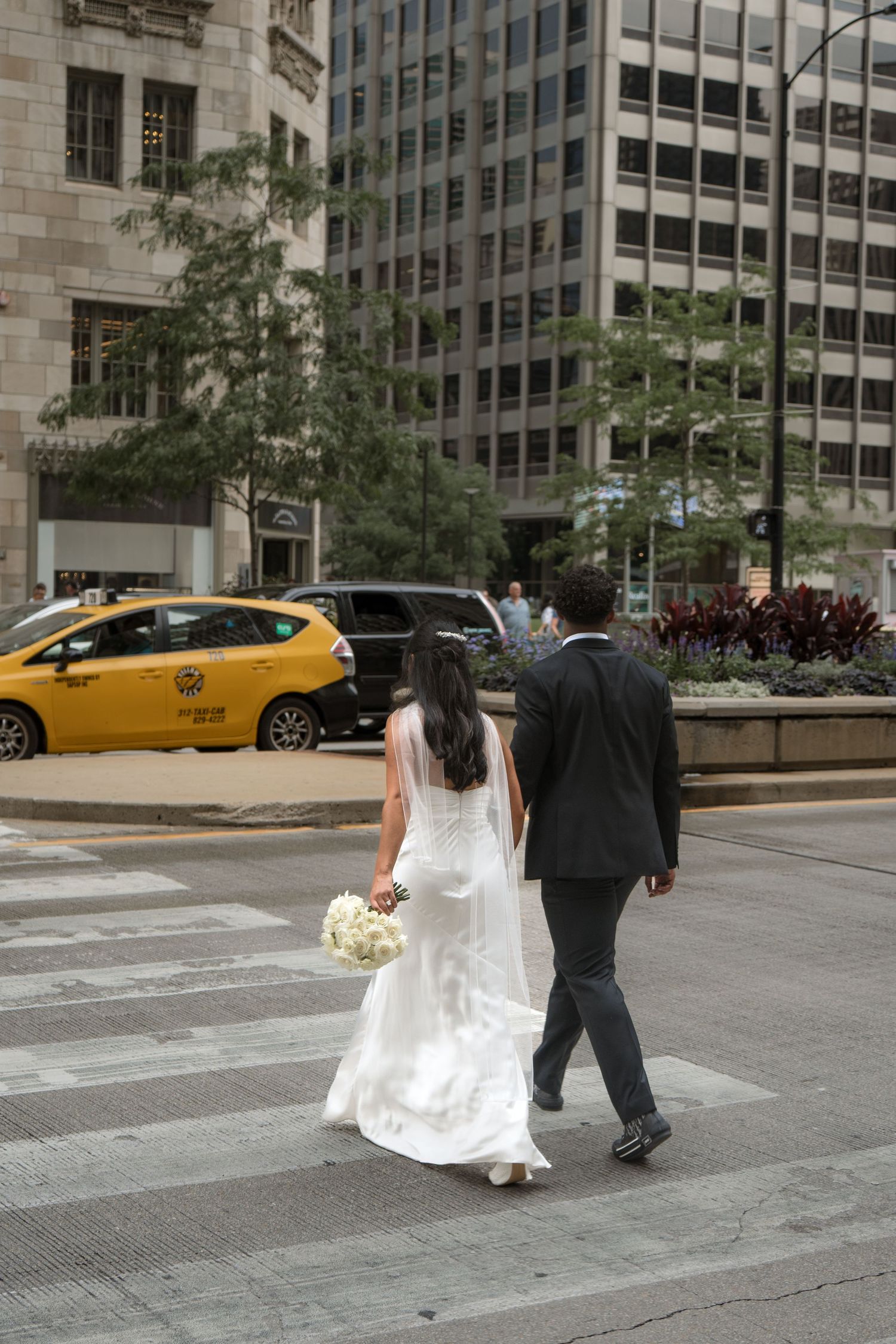 Bride and groom walking across a crosswalk in Chicago with a yellow taxi cab visible in the background.