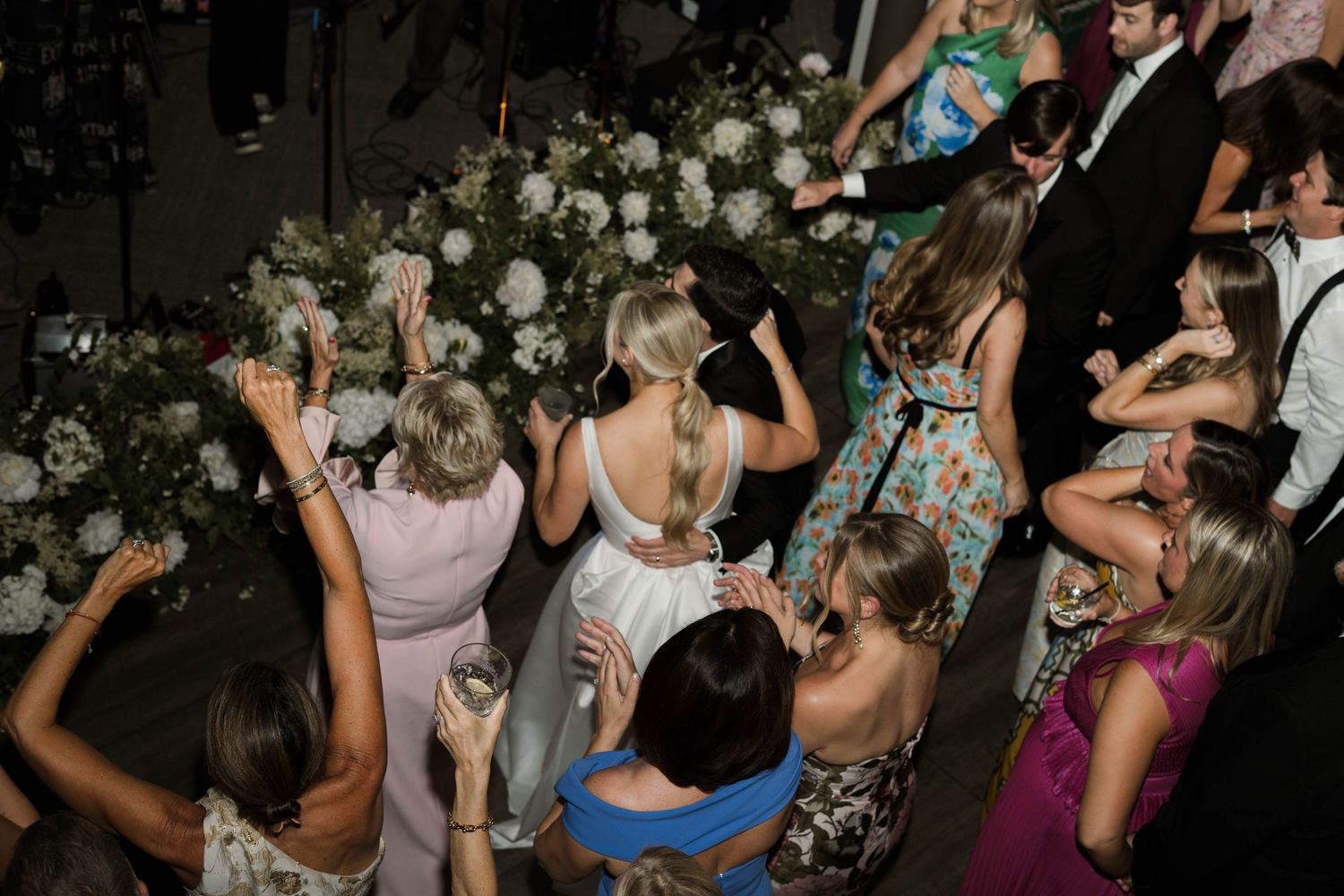 Guests dancing joyfully at an elegant wedding reception with floral arrangements and colorful formal attire.