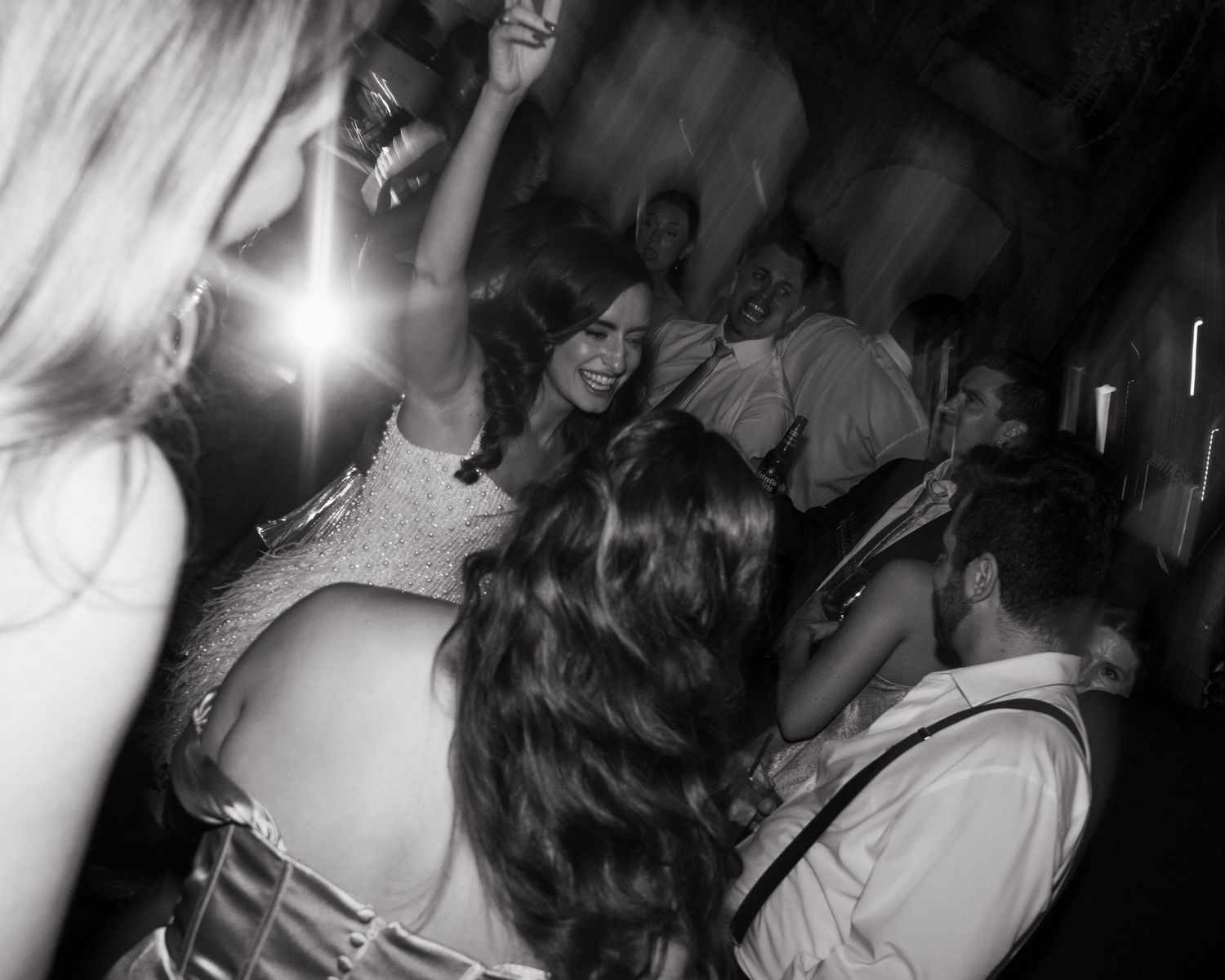 Black and white photo of people dancing and celebrating at a lively party or wedding reception.