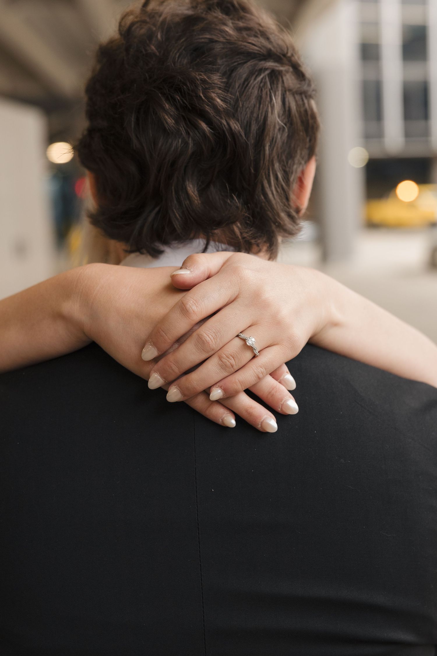 Close-up of a woman's hand with an engagement ring resting on a man's shoulder during a romantic embrace.