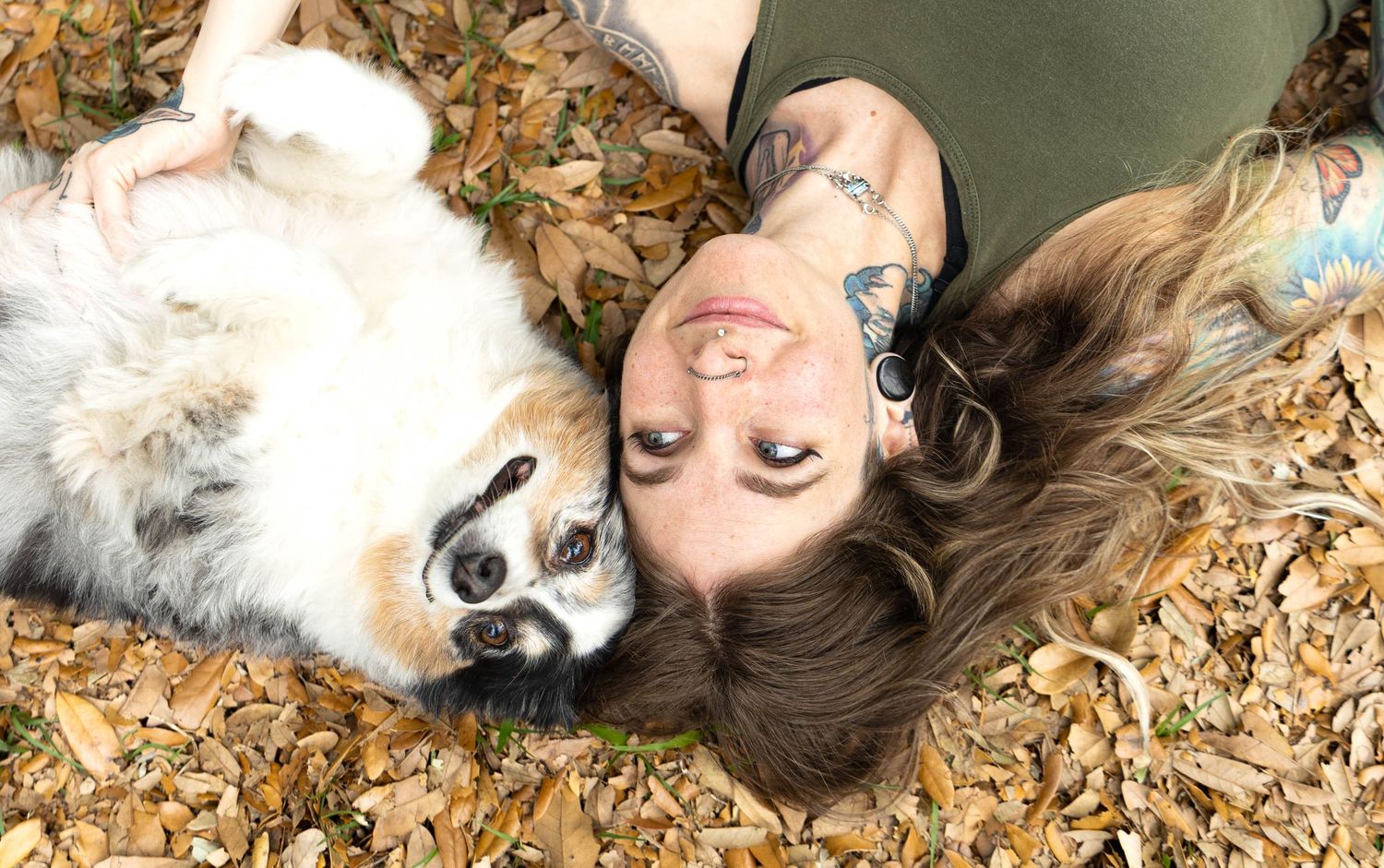 Pet and owner lying in fallen autumn leaves, smiling at the camera during an Orlando pet portrait session, warm and natural connection.