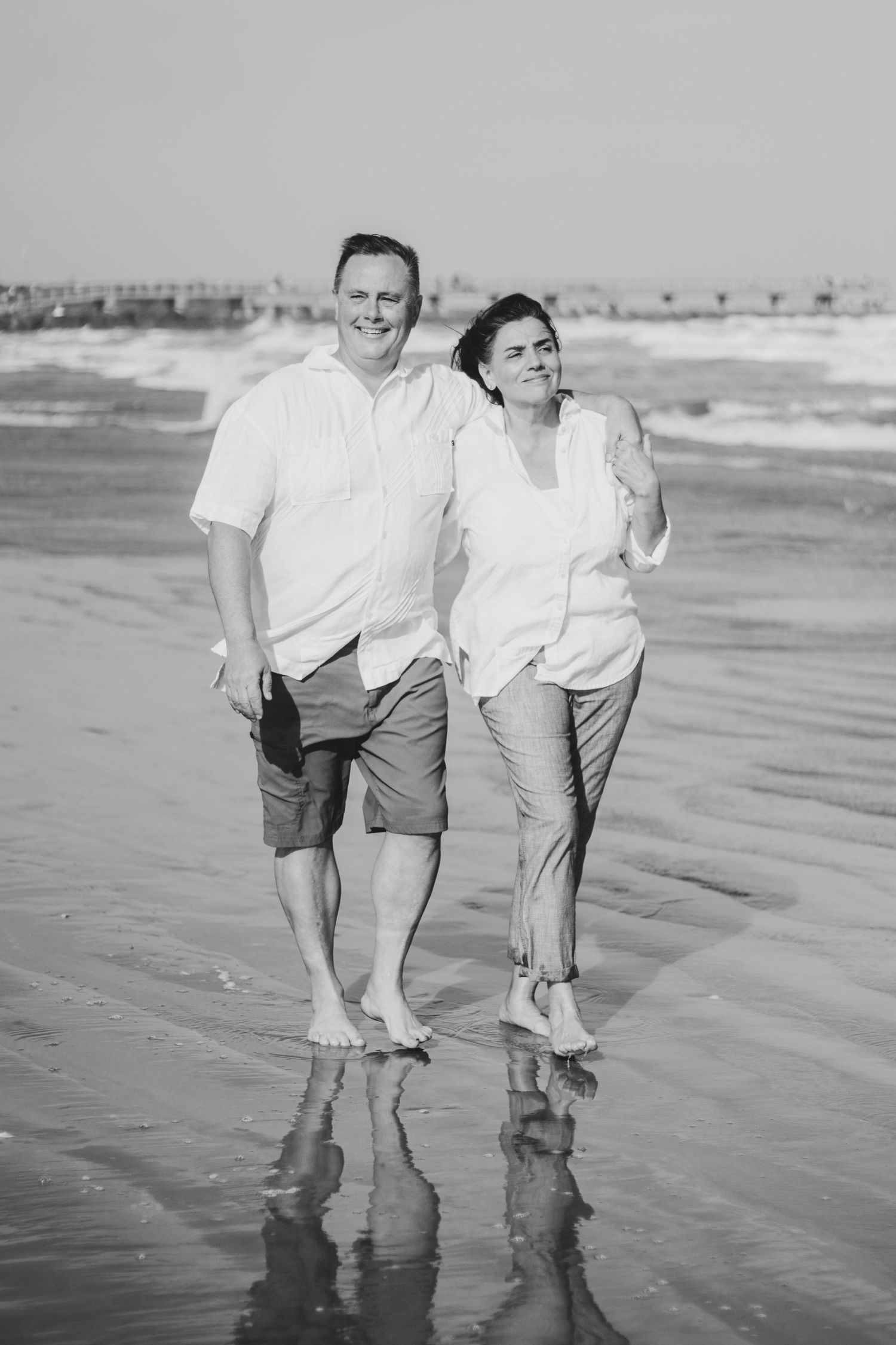 Couple holding hands while walking along the shore during a sunset anniversary beach portrait session.