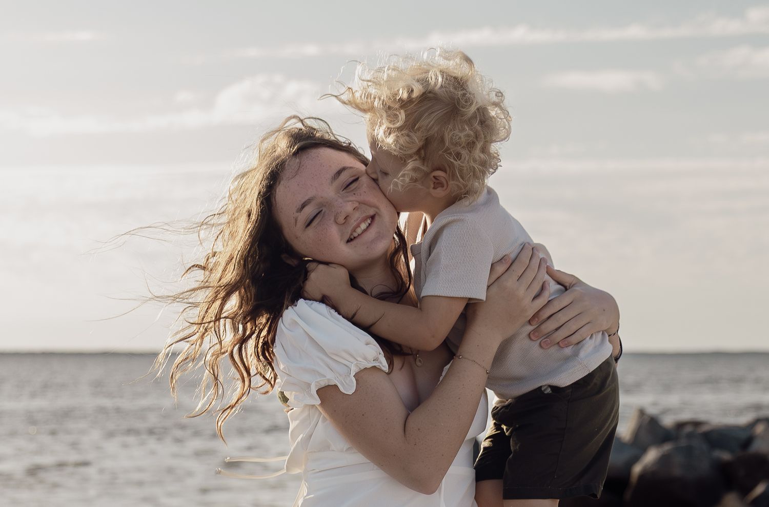 Toddler boy hugging and kissing his older sister during a warm sunset beach family session, natural Orlando family lifestyle portrait.