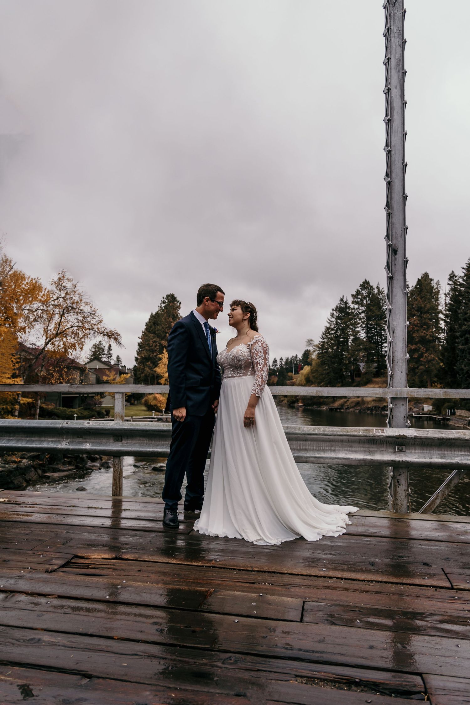Bride and groom share a romantic moment on a wooden dock by a lake on a cloudy autumn wedding day.