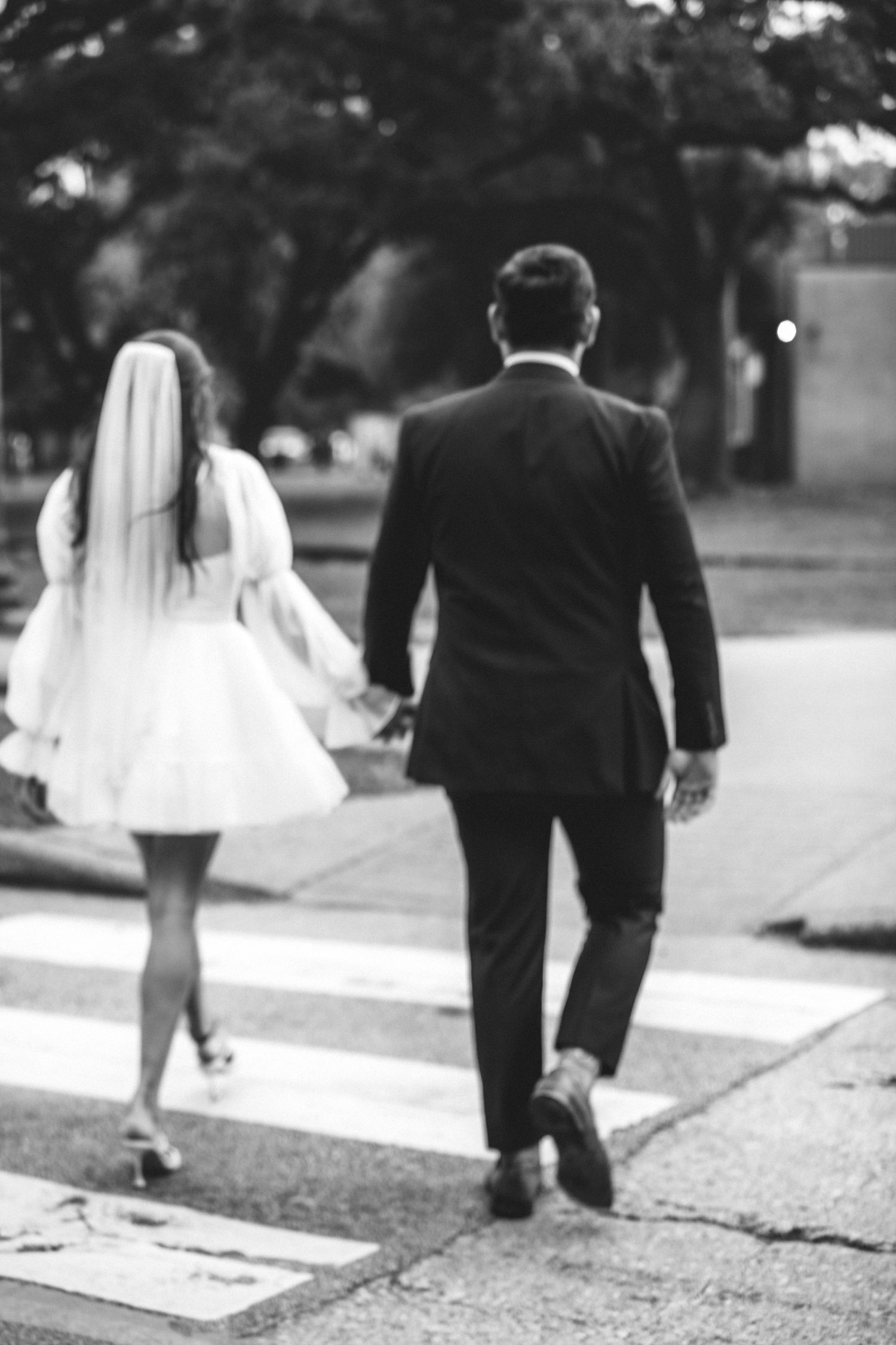 Bride and groom walk hand in hand across a crosswalk in black and white wedding photo.