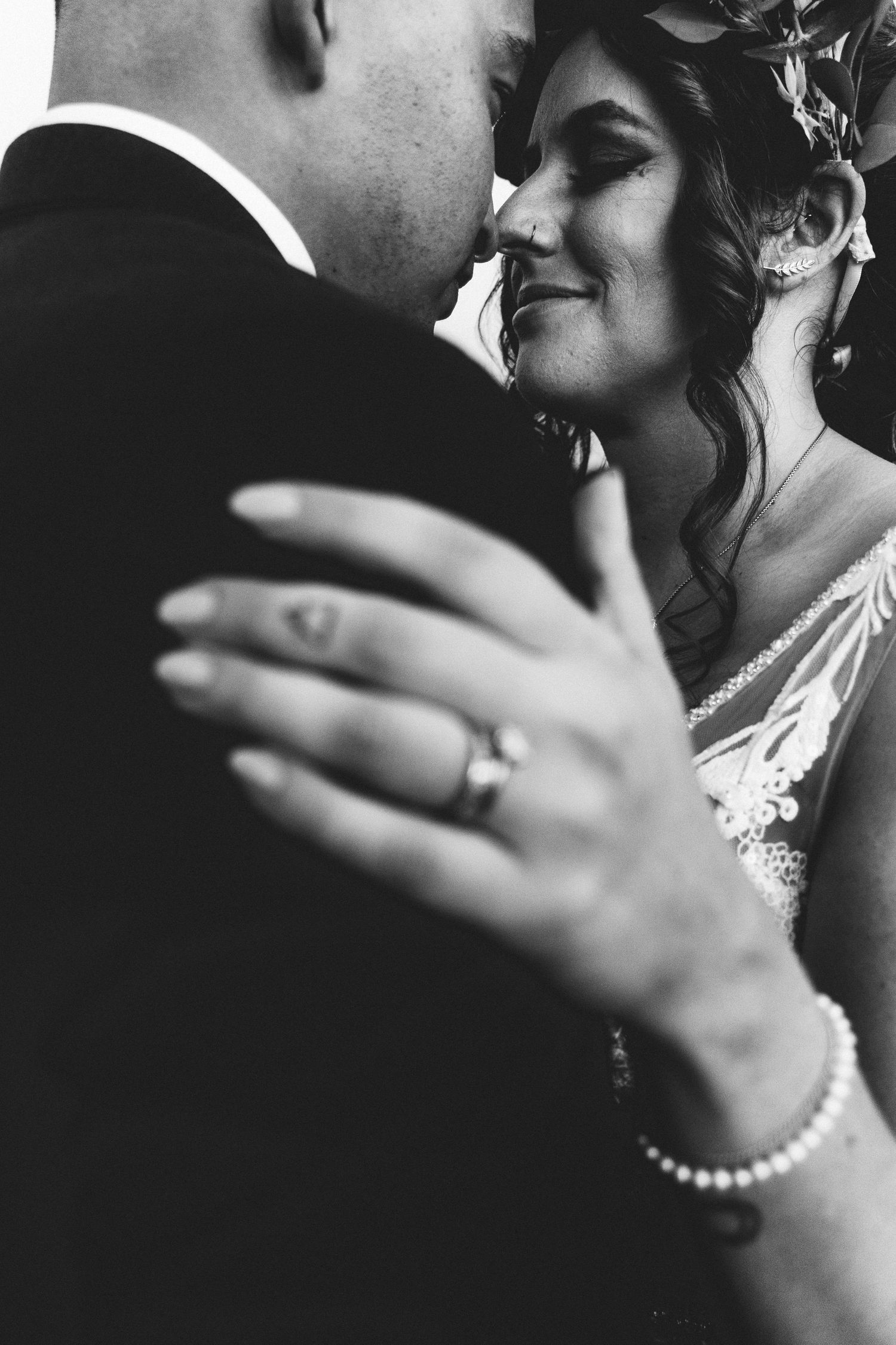 Black and white close-up of a smiling bride embracing her groom, showcasing her diamond engagement ring.