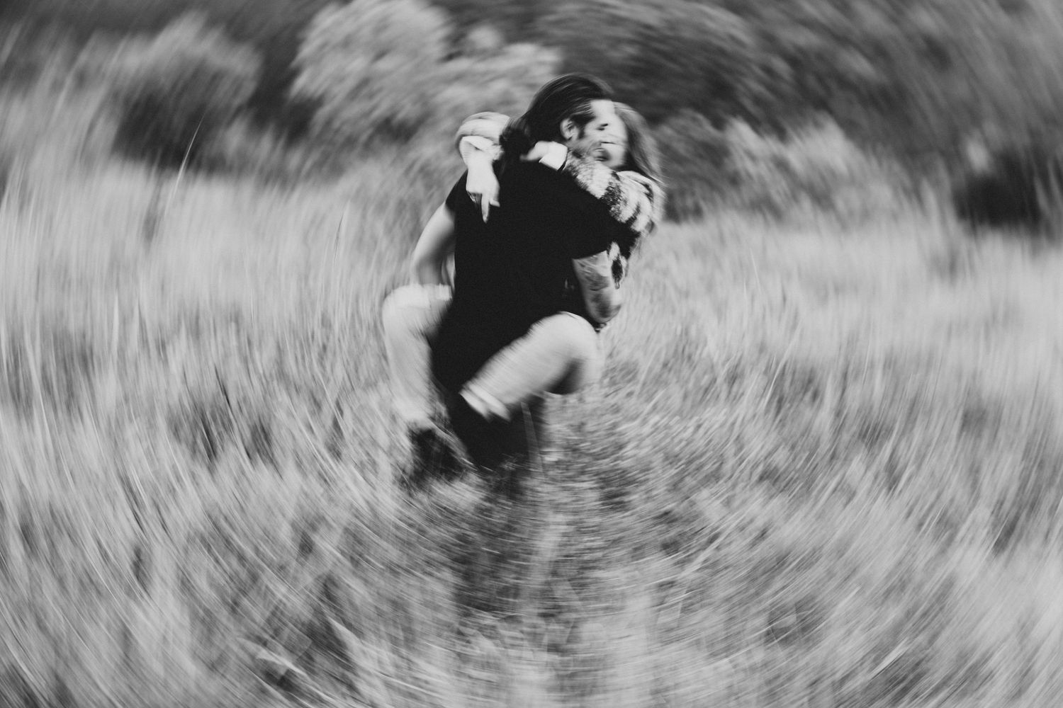 Black and white photo of a couple embracing and spinning in a field with a dreamy blur effect.