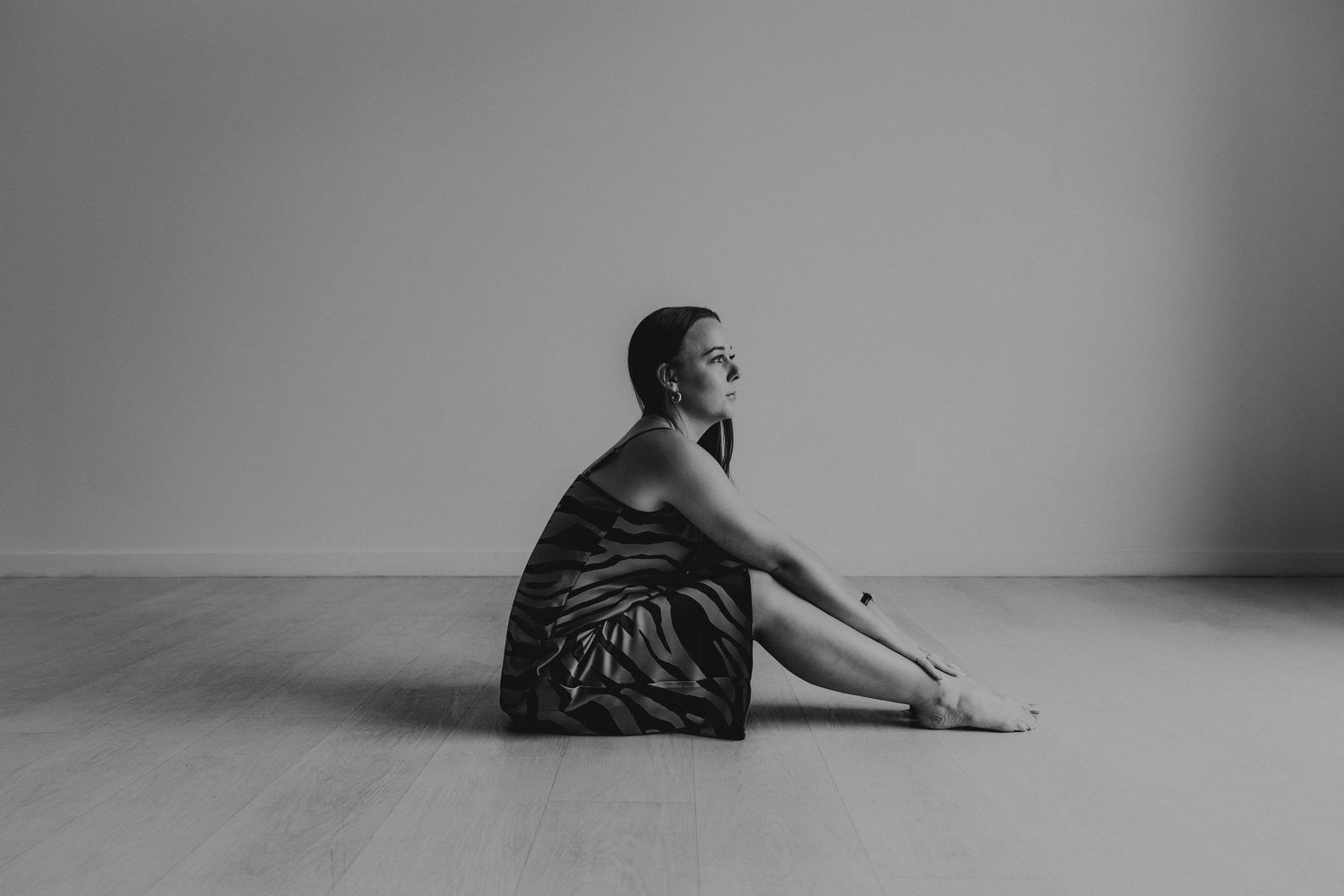 Black and white photo of a woman in a satin dress sitting gracefully on a studio floor.