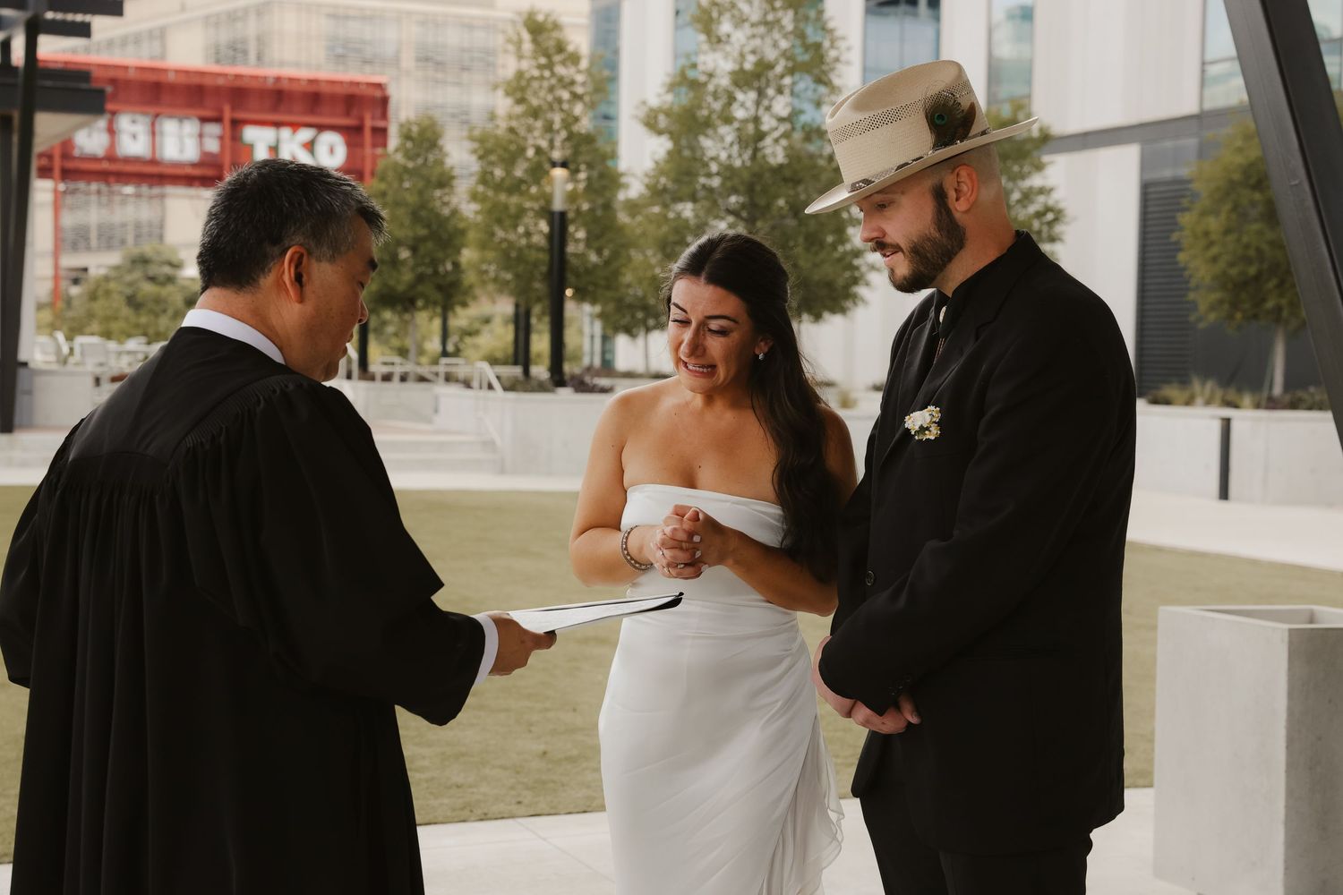 Smiling bride in white dress stands with groom in cowboy hat during outdoor elopement ceremony.