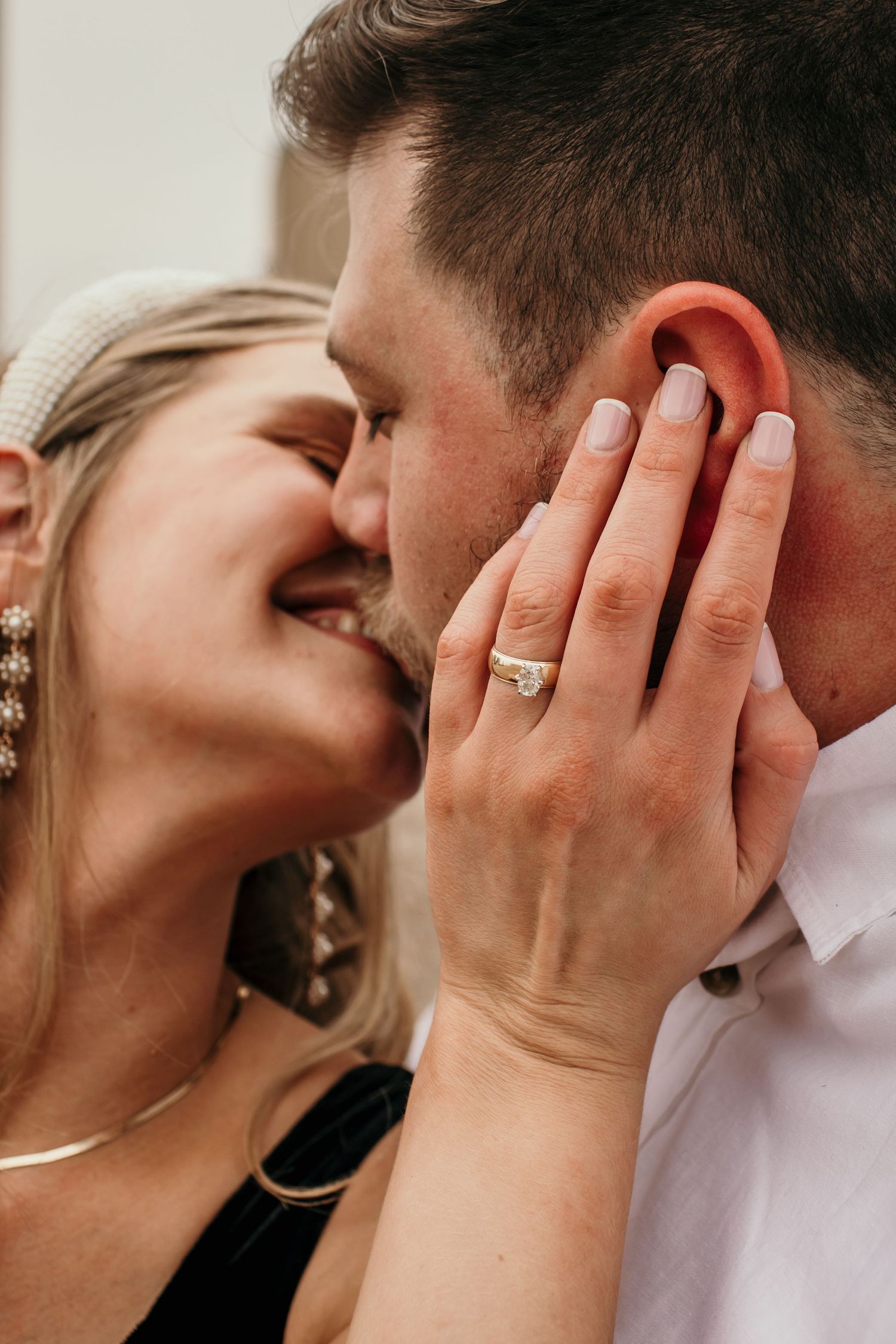 Close-up of smiling couple nearly kissing, woman displaying diamond engagement ring on his cheek.