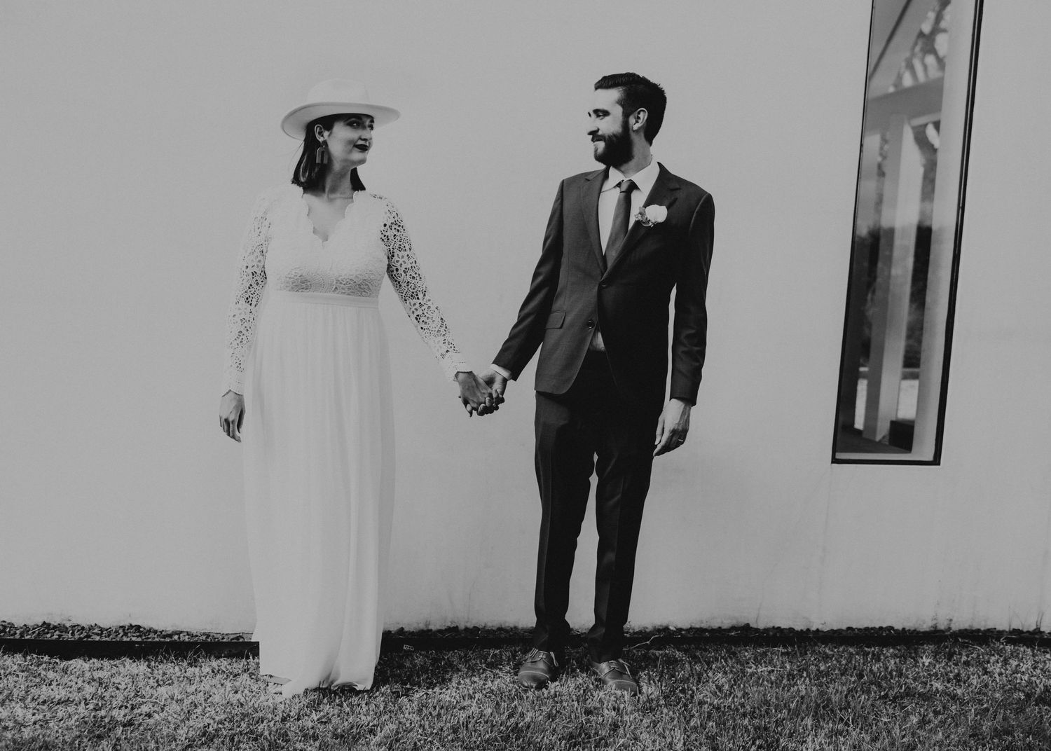 Black and white photo of a bride in white gown and groom in dark suit holding hands at their wedding.