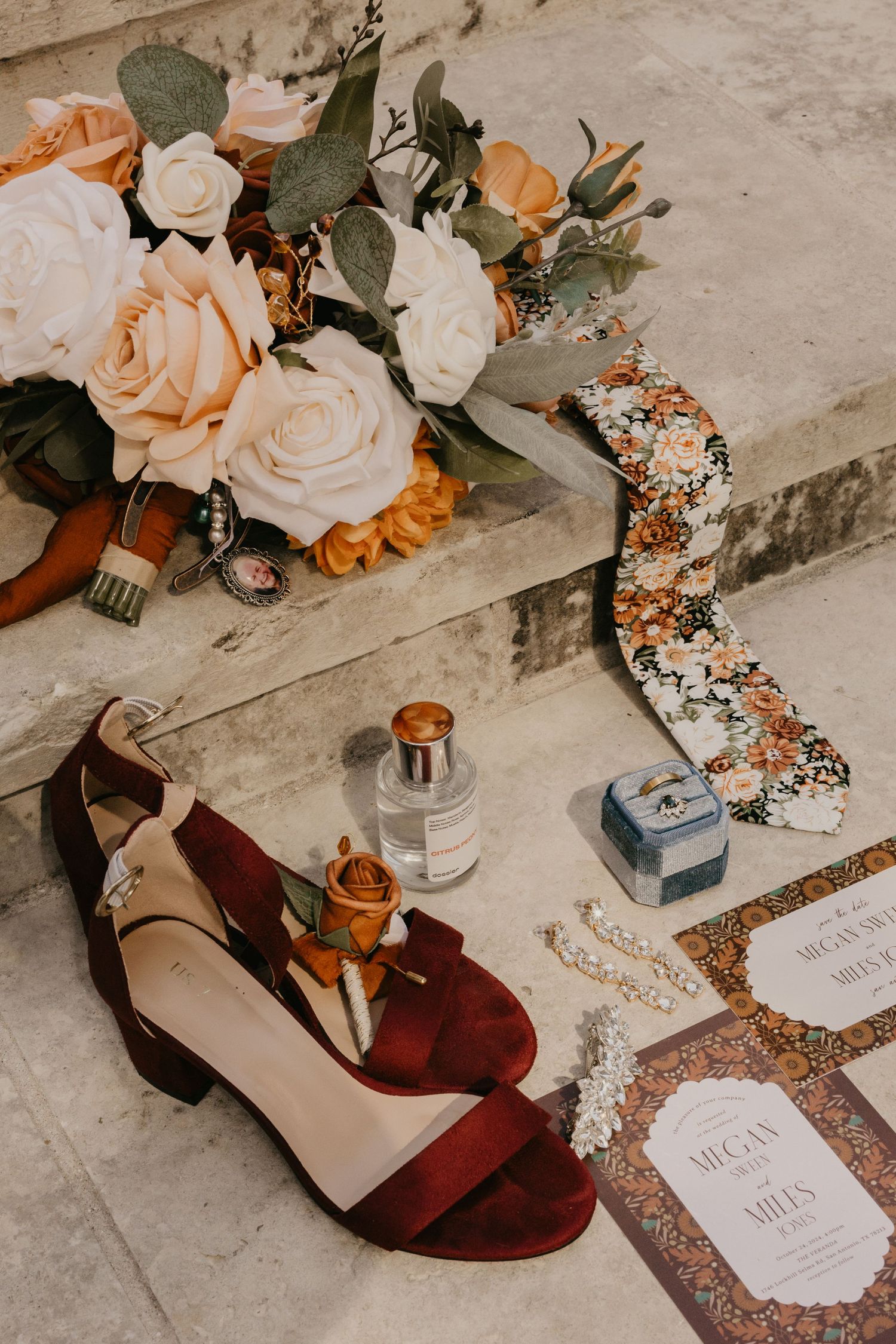 Flat lay of wedding details including red heels, floral bouquet, perfume, and invitation suite.