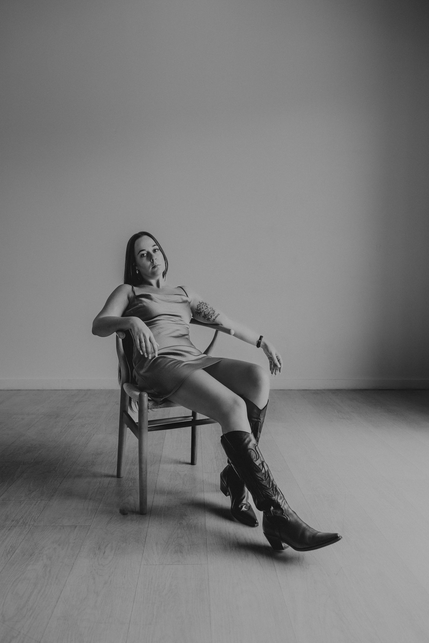 Black and white portrait of a woman relaxing on a chair wearing cowboy boots and a dress.