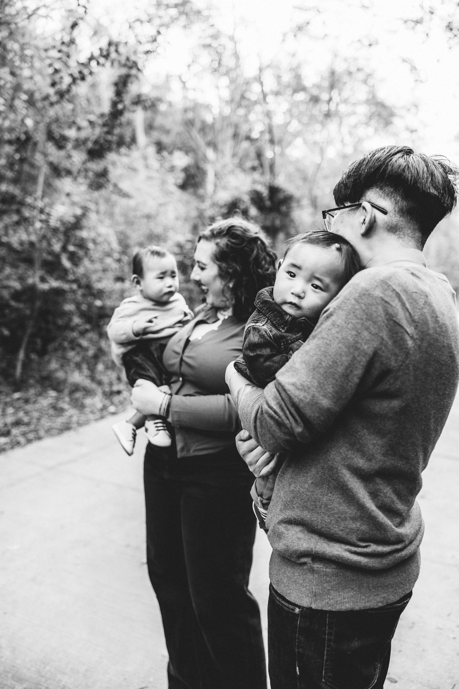 Black and white family portrait of parents each holding a baby on a scenic outdoor pathway.
