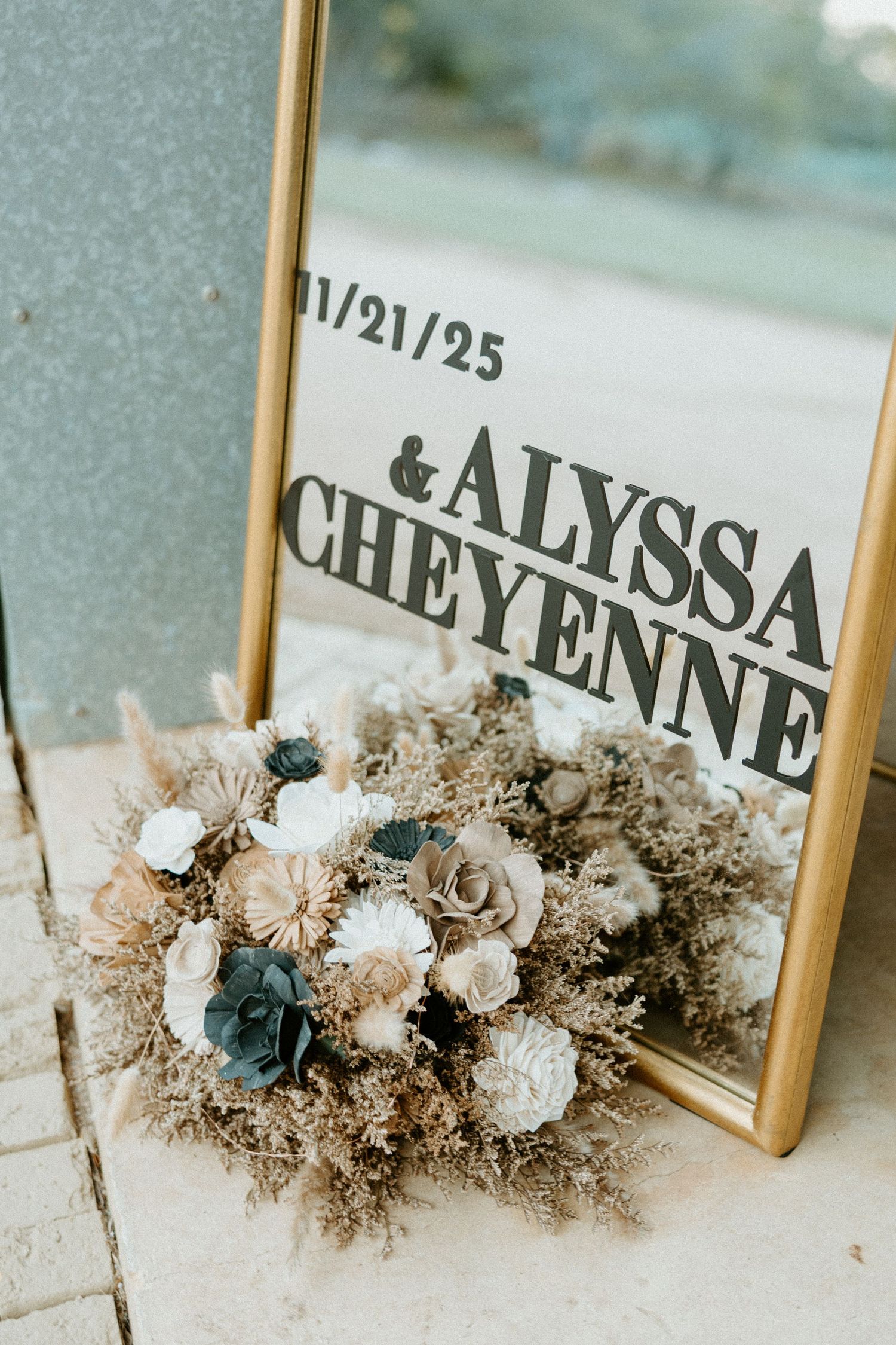 Wedding mirror sign reading Alyssa and Cheyenne 11/21/25 decorated with dried floral arrangement.