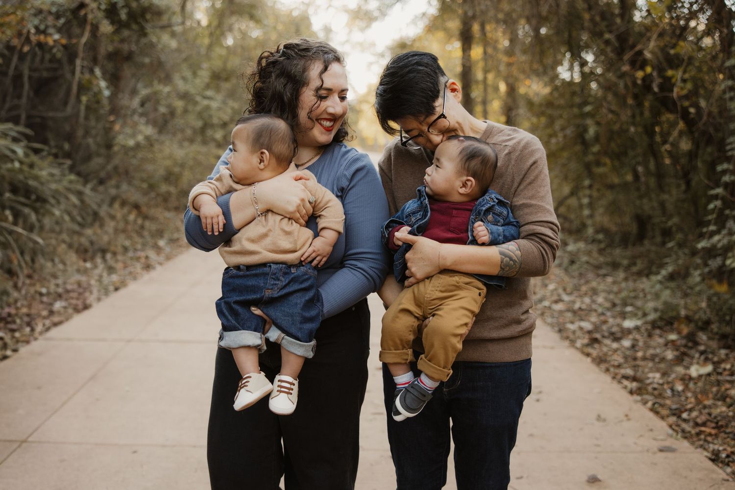Happy family with two parents leaning toward each other while holding their twin baby boys outdoors.