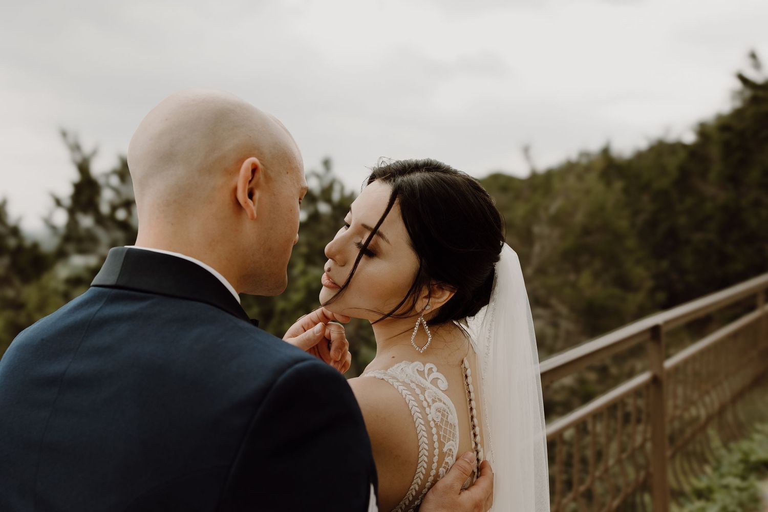 Groom tenderly holds brides face as she smiles in a close romantic portrait on their outdoor wedding day.